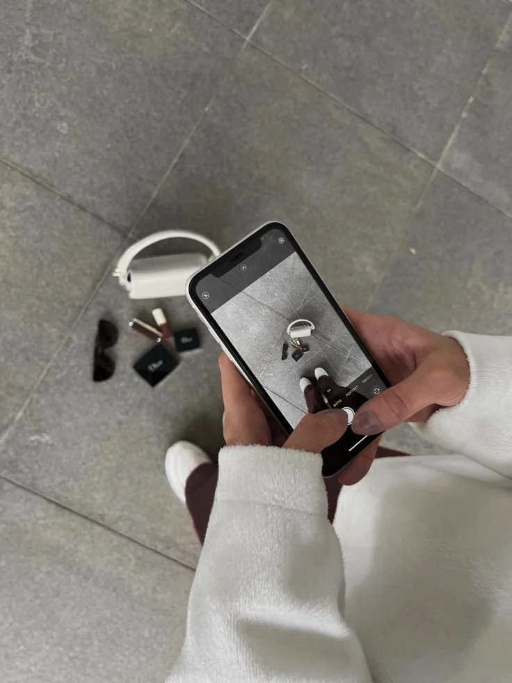 Person taking a photo of makeup and accessories on the floor with a smartphone.