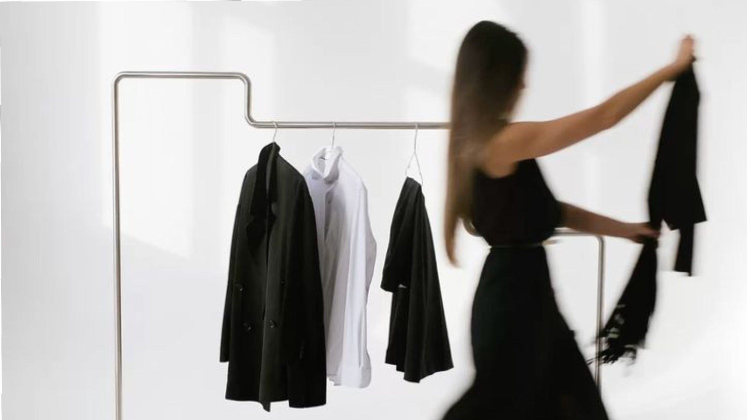 A woman in black clothing is hanging a black garment on a clothing rack with black and white dresses.