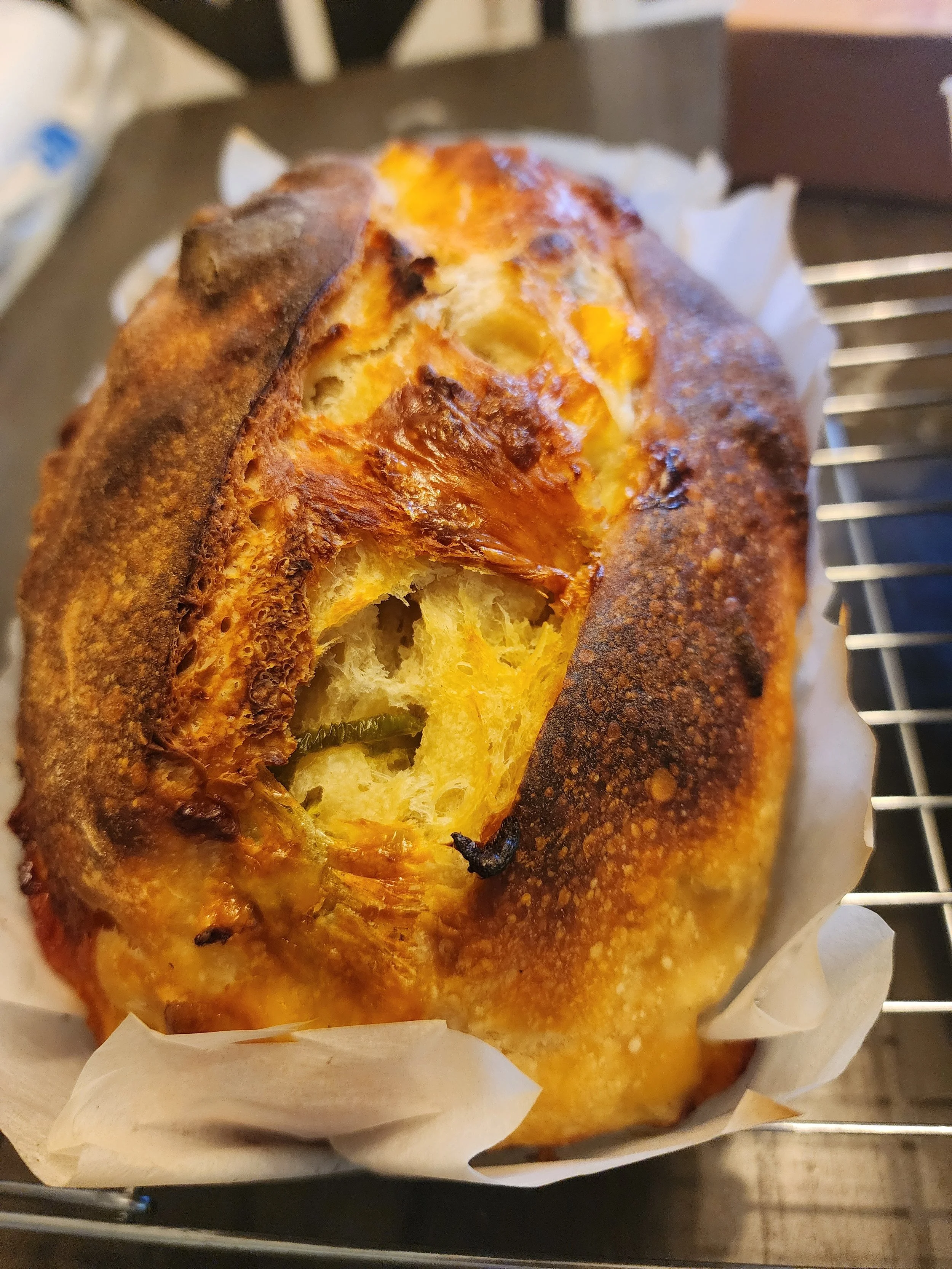 A partially eaten loaf of bread with a golden-brown crust, resting on parchment paper on a cooling rack.