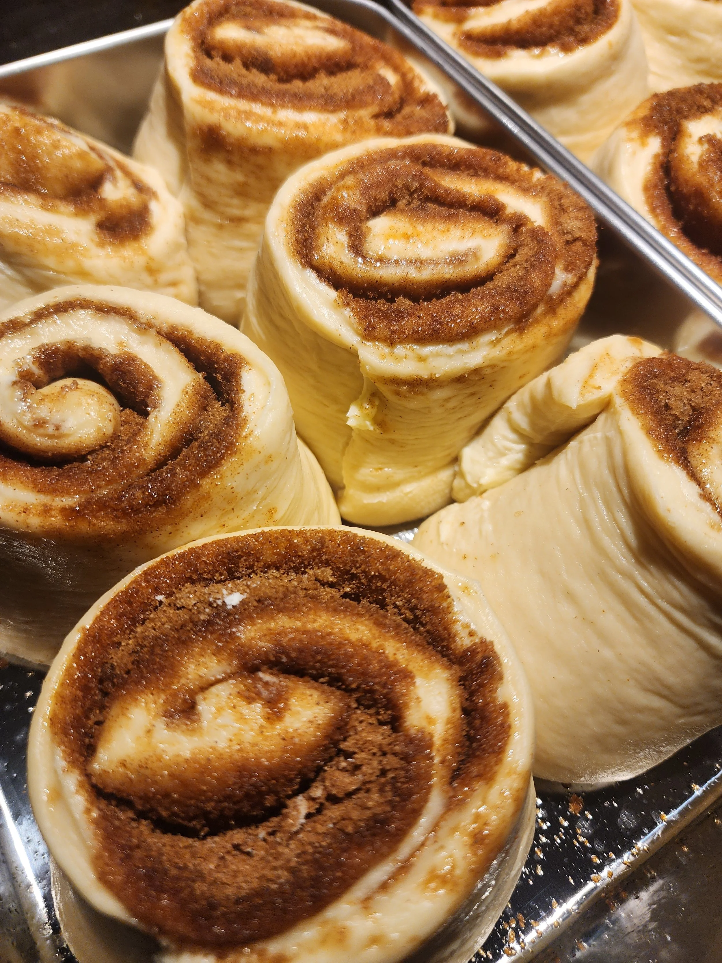 Close-up of cinnamon rolls in a metal baking dish, showing swirls of cinnamon and icing.