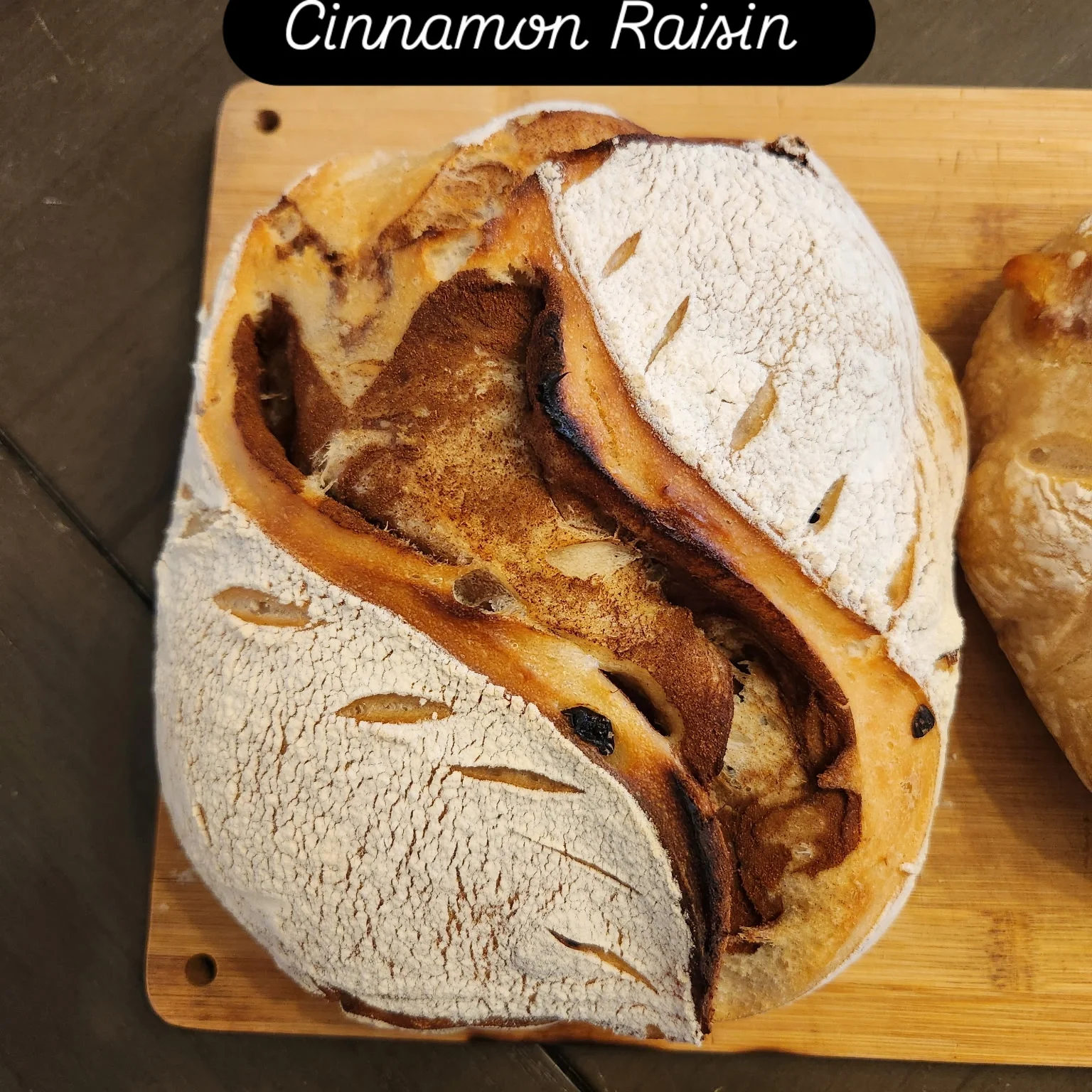 A round cinnamon raisin bread loaf with a dusting of flour on top, placed on a wooden cutting board.