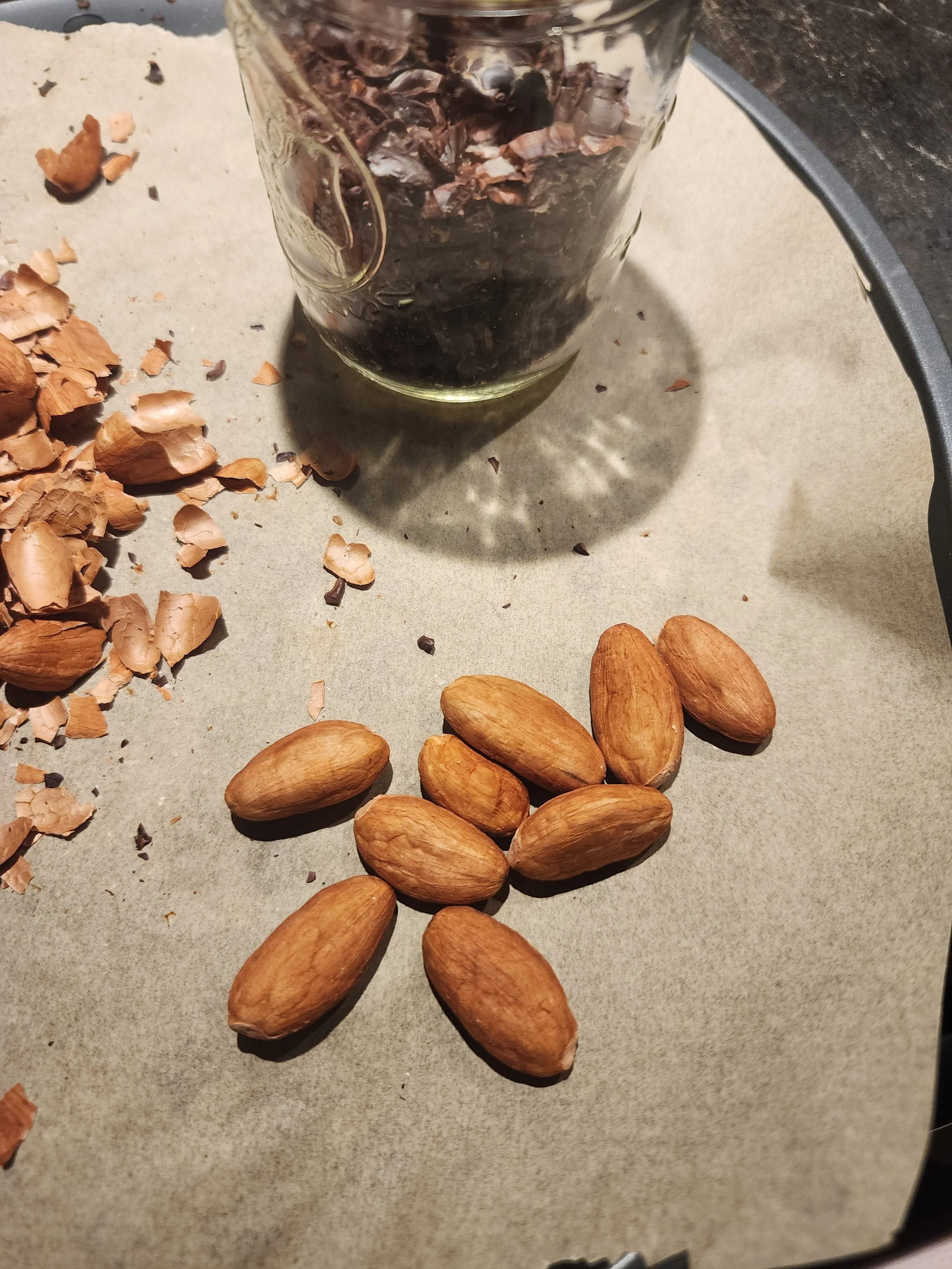 A glass of cola on a table with almonds and peanut shells scattered around.