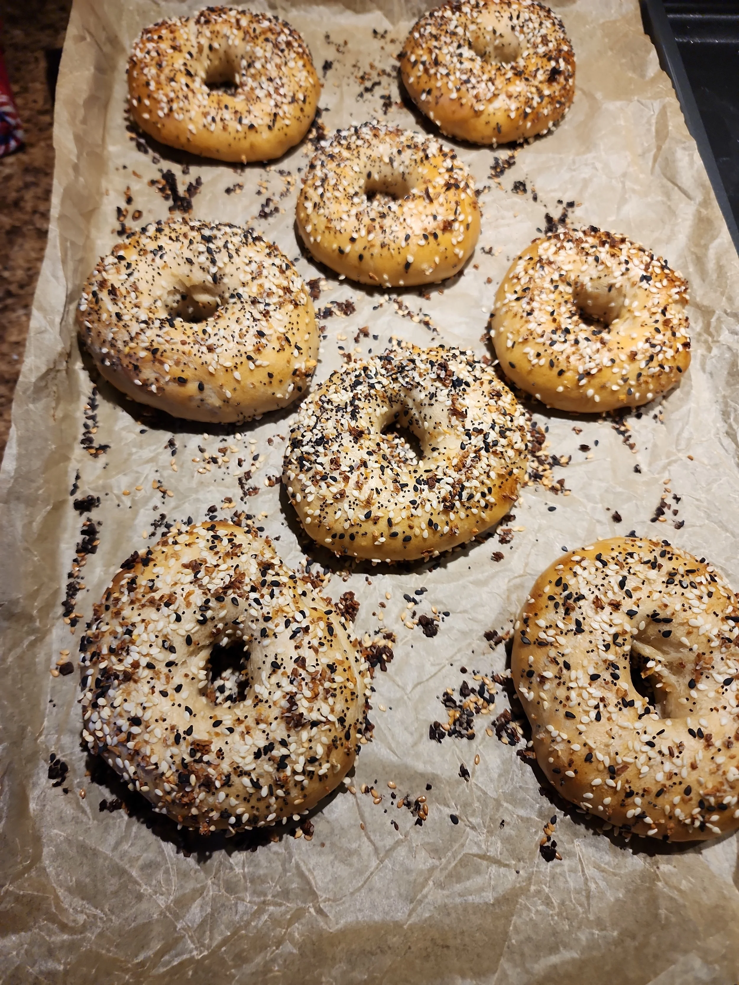 Six bagels topped with various seeds and spices on baking paper.