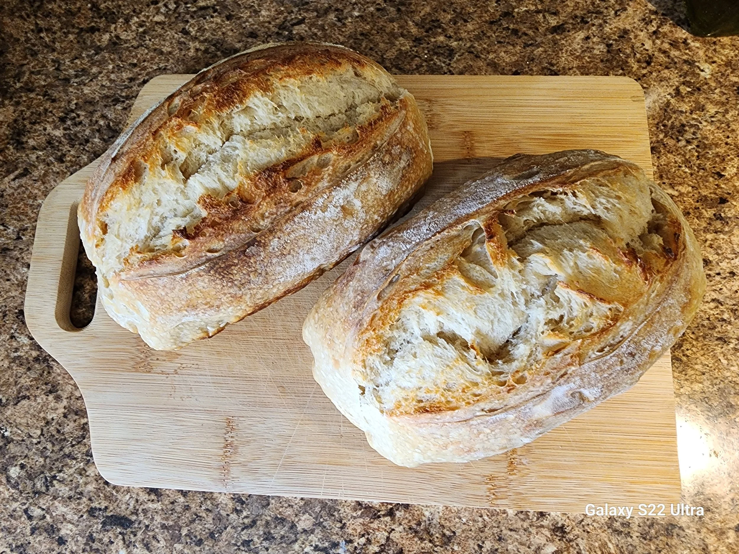 Three pieces of bread on a wooden cutting board, placed on a speckled granite countertop.