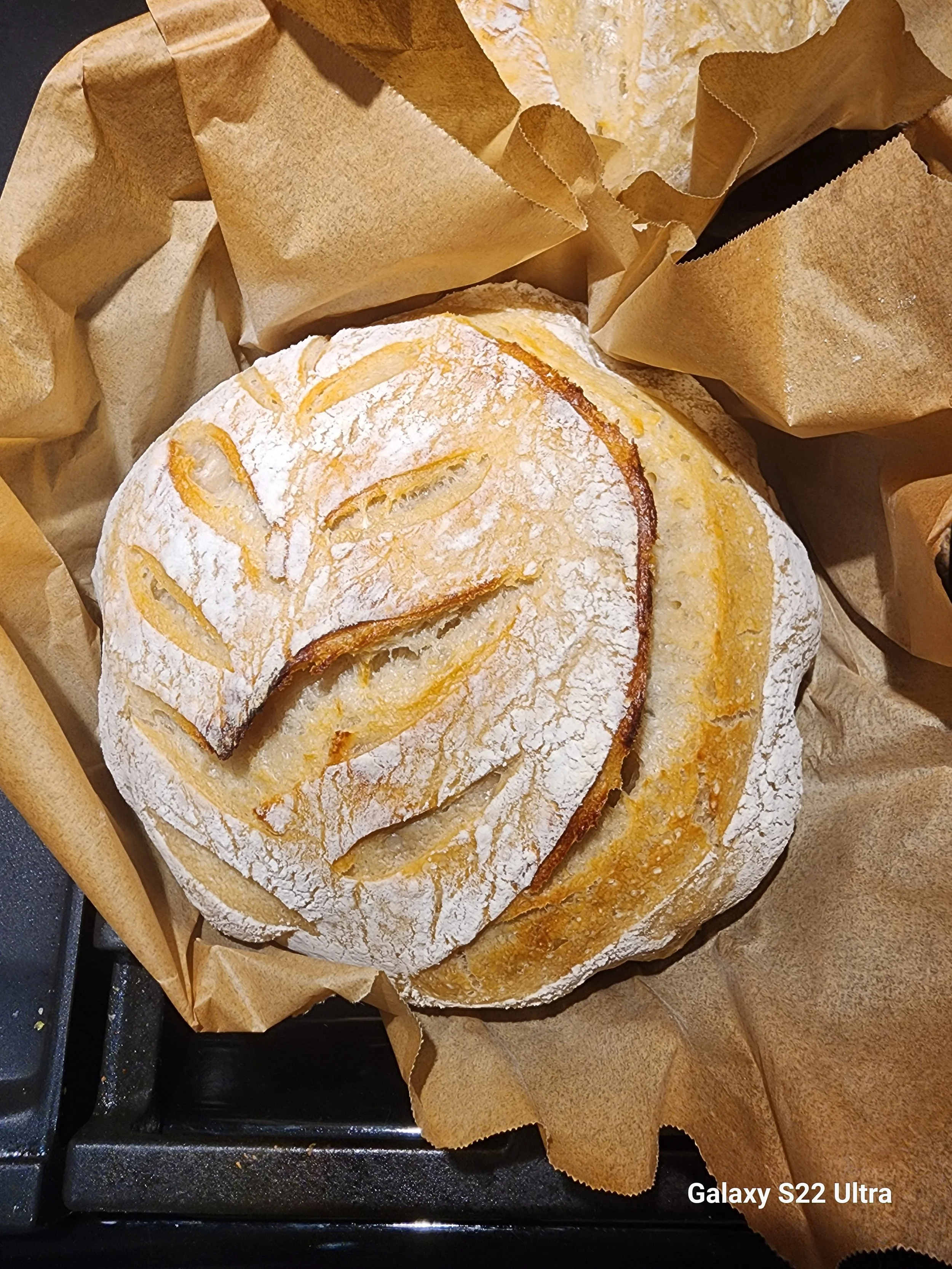 A round baked bread dusted with powdered sugar, placed on brown parchment paper.