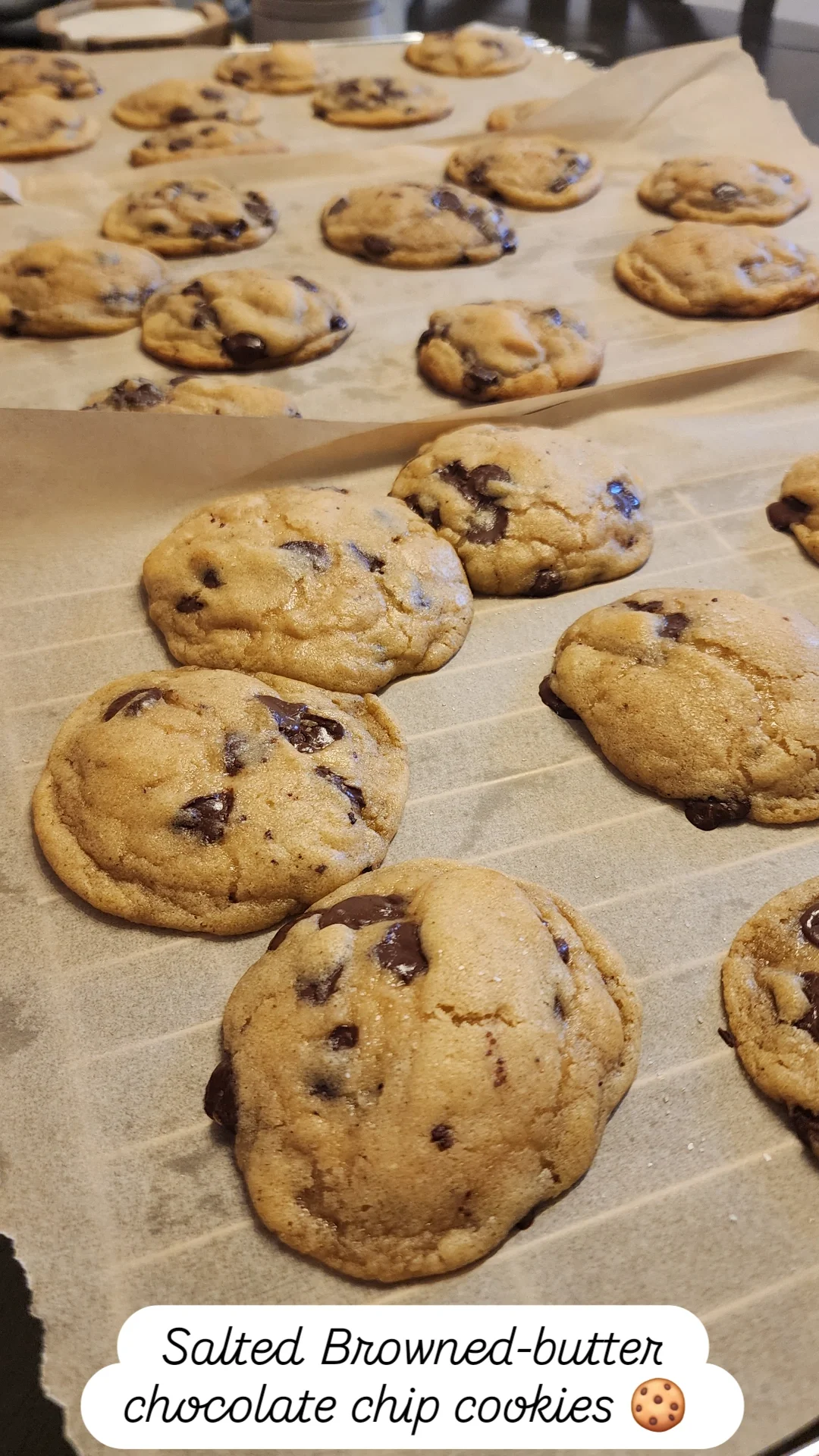 A tray of freshly baked salted browned-butter chocolate chip cookies on parchment paper.