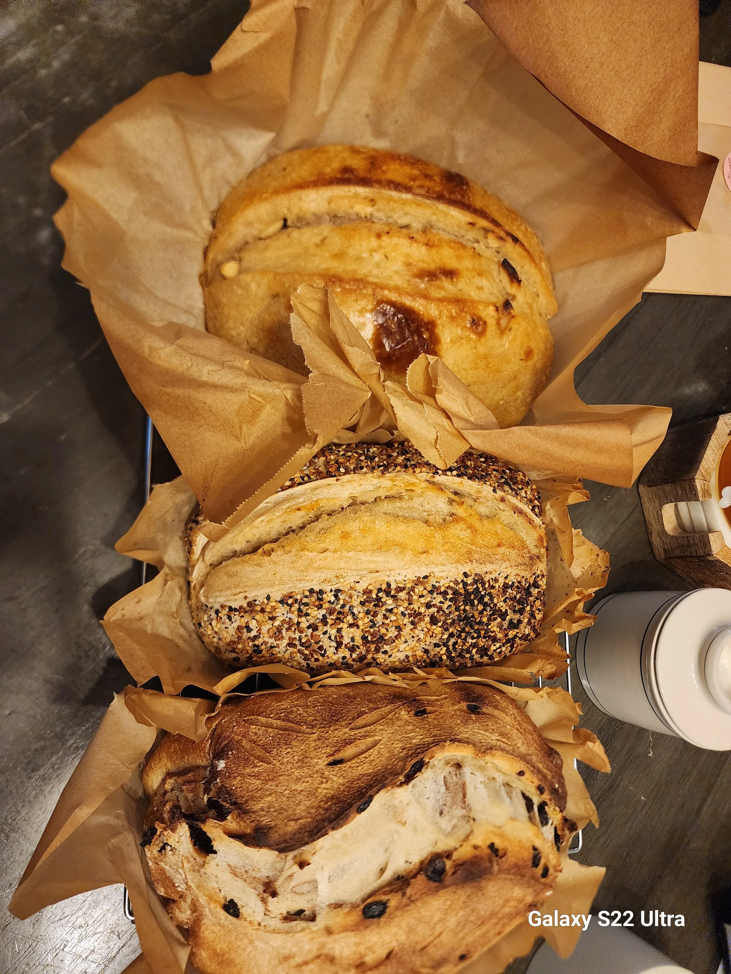 A top-down view of various loaves of bread wrapped in parchment paper, including a multigrain loaf with seeds on top and a baguette.