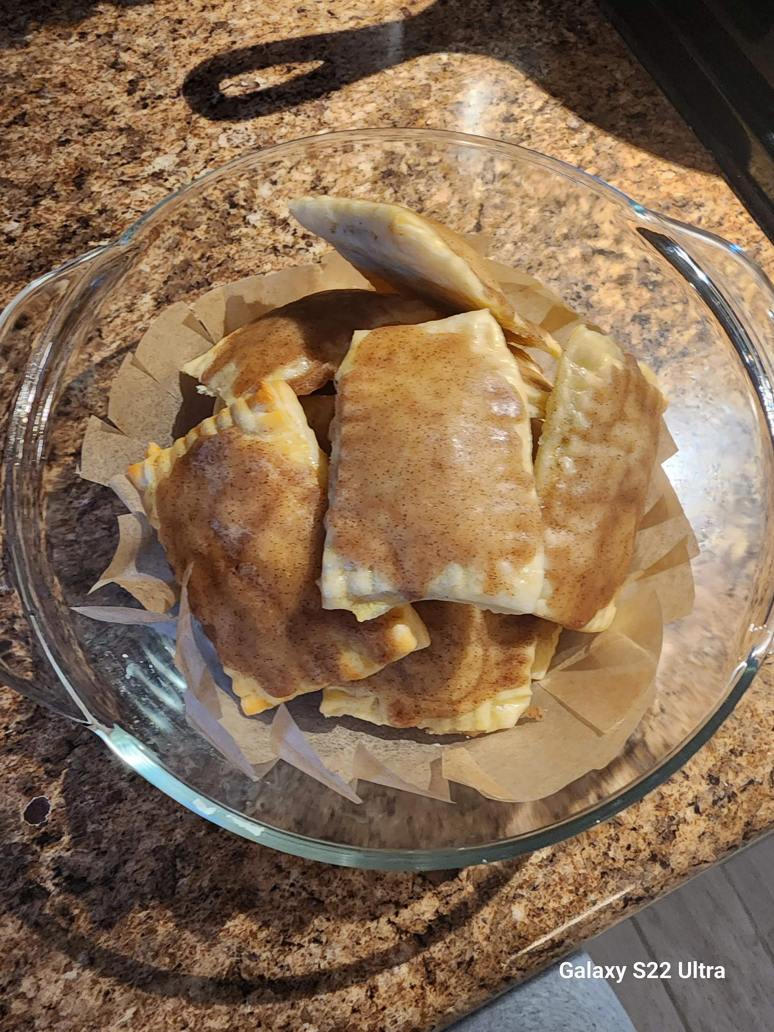 A glass bowl containing slices of baked apple with cinnamon, placed on a kitchen countertop.
