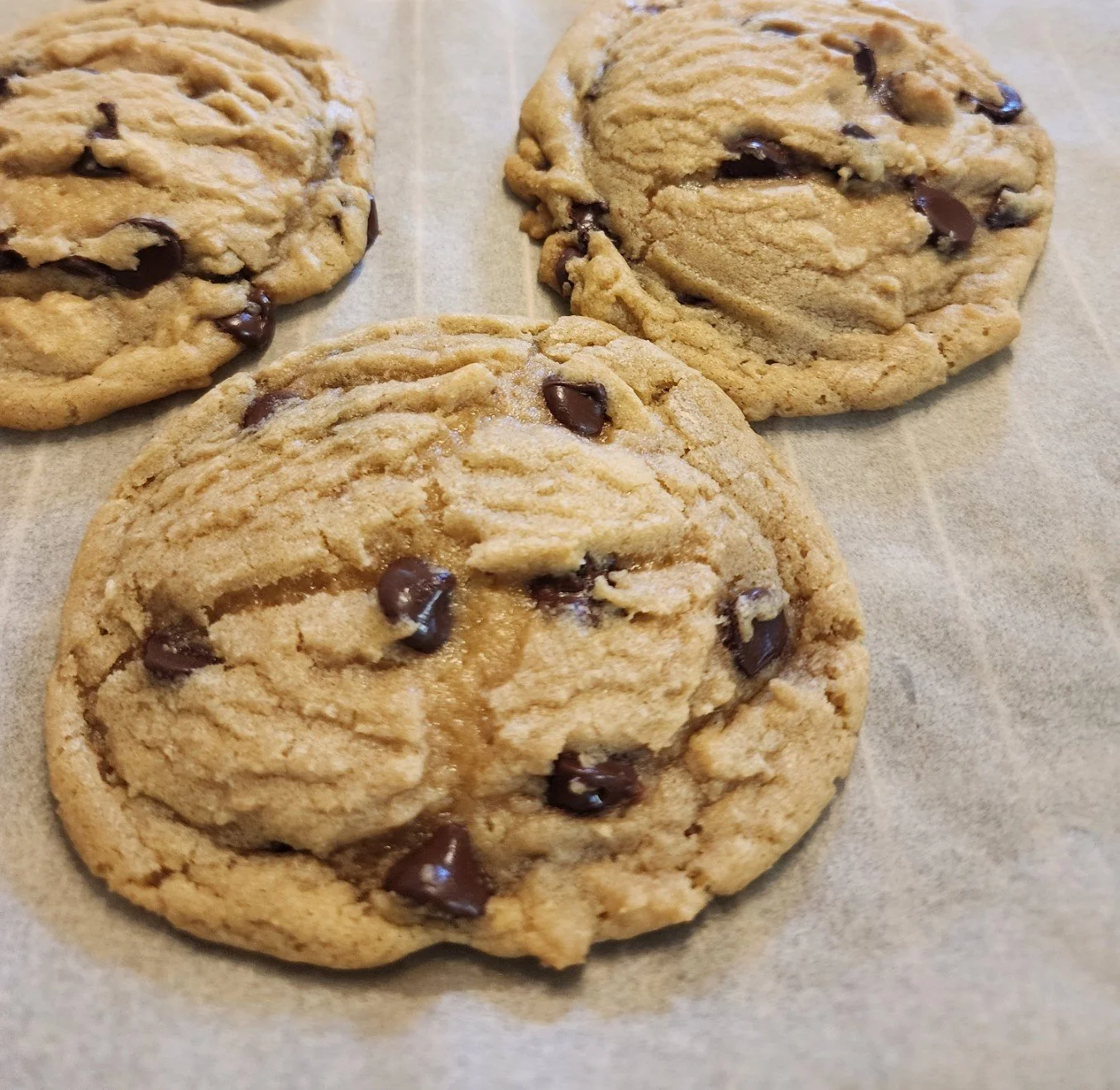 Three chocolate chip cookies on parchment paper.