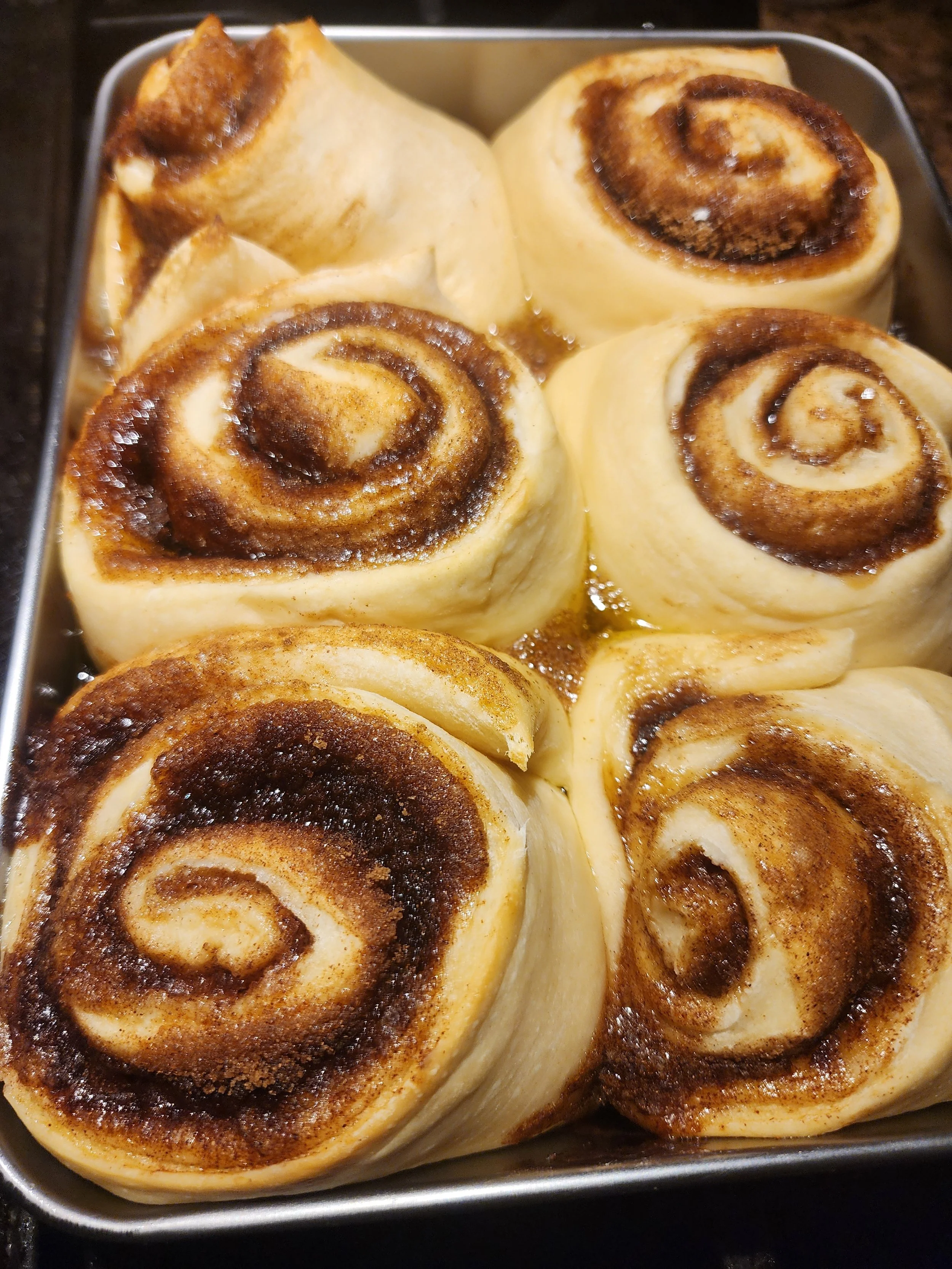 Close-up of four cinnamon rolls in a baking dish, showing swirl patterns and golden-brown tops.