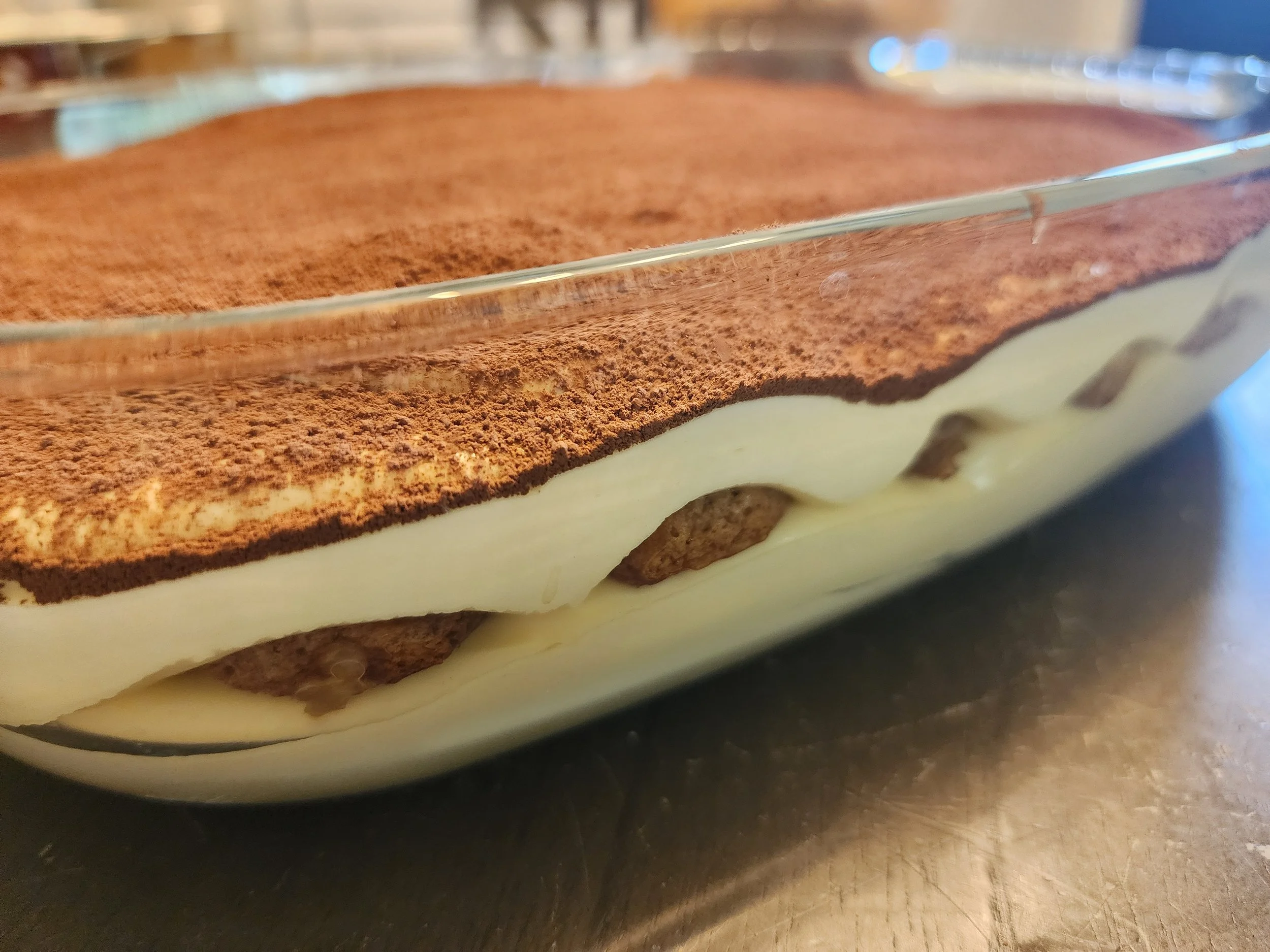 Layered dessert with whipped cream, chocolate, and crust in a glass dish on a dark surface.