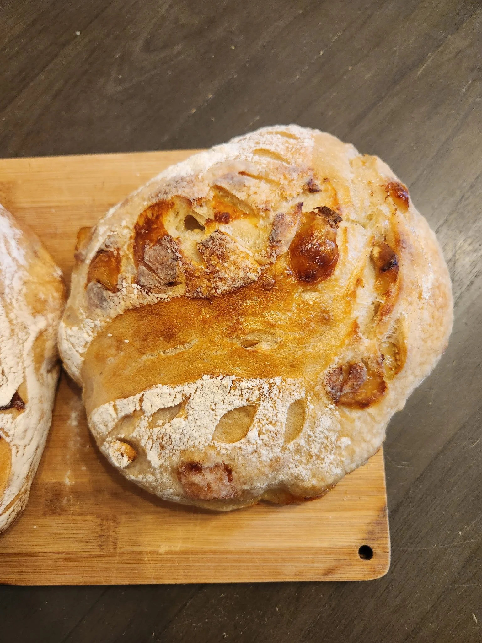 A loaf of artisan bread with a crusty, golden exterior and a dusting of flour on top, resting on a wooden cutting board.