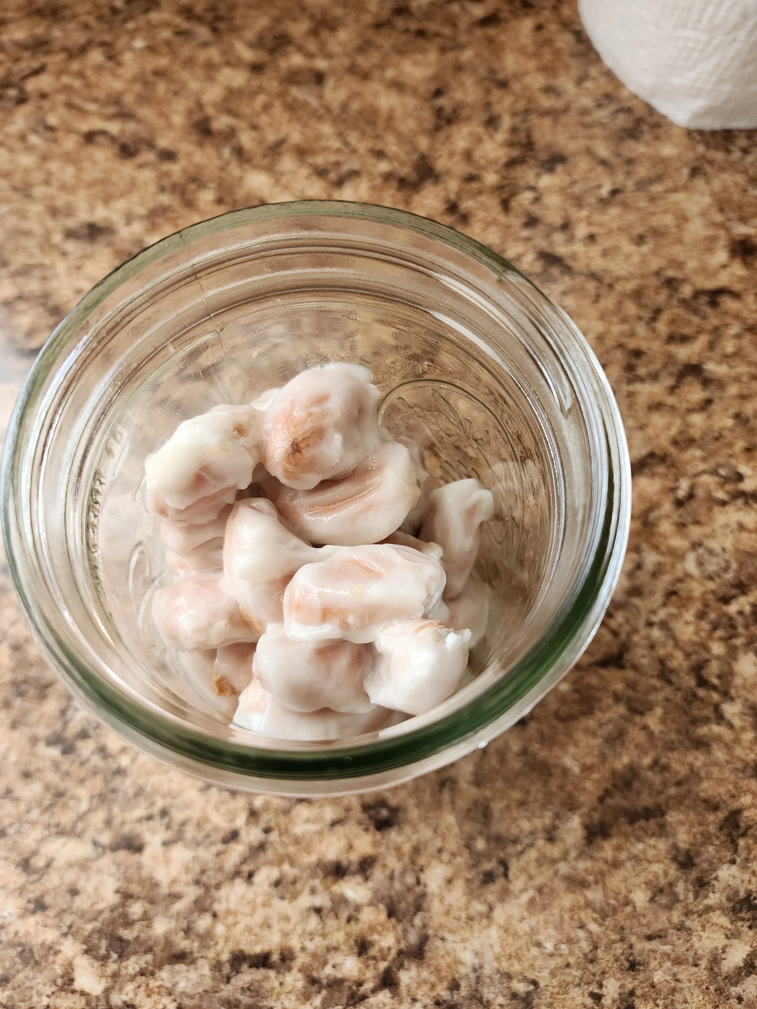 Close-up of a jar filled with bananas in a creamy sauce on a brown speckled countertop.
