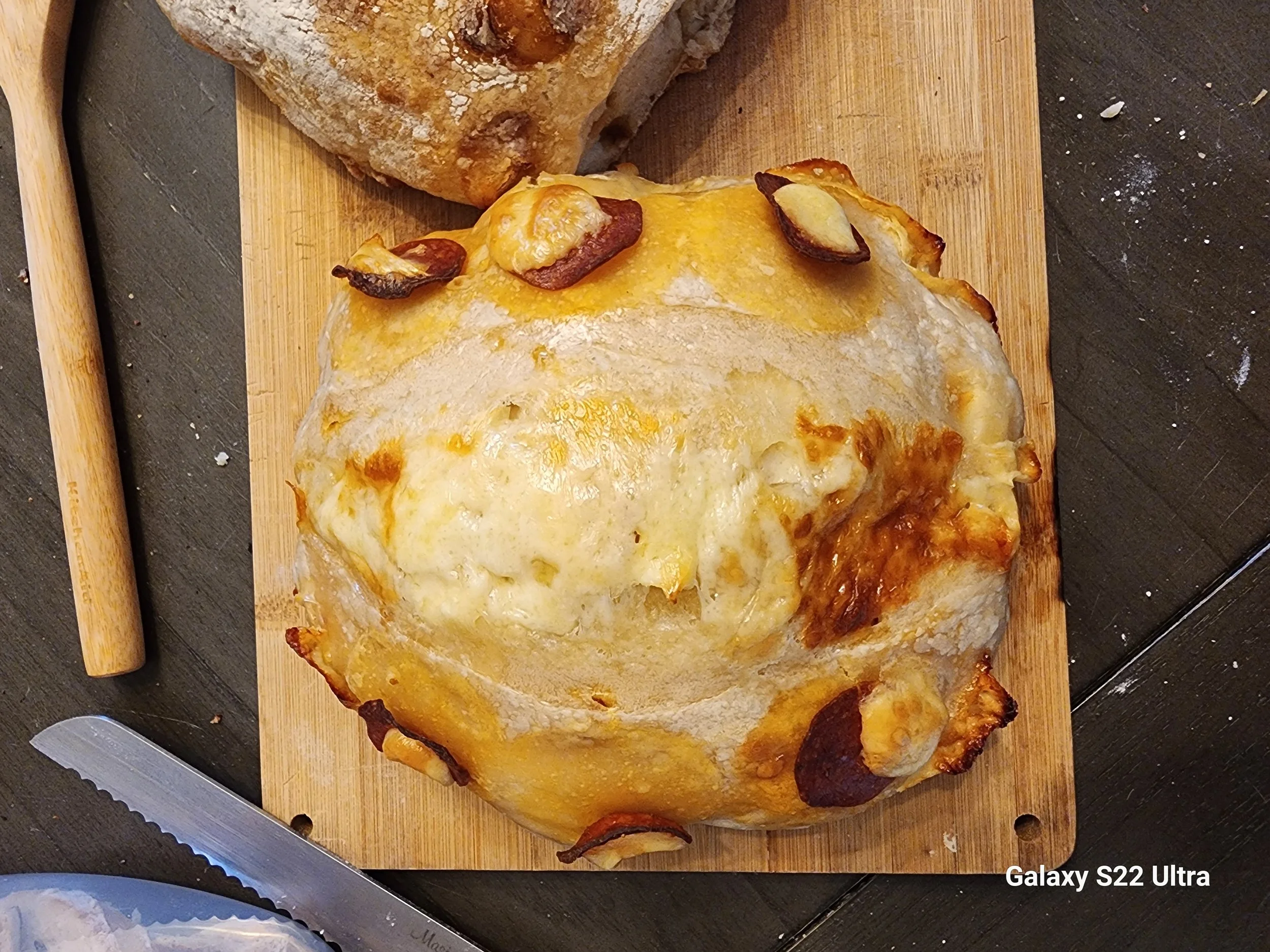 Baked calzone or stromboli with melted cheese and pepperoni, on a wooden cutting board with a bread knife nearby.