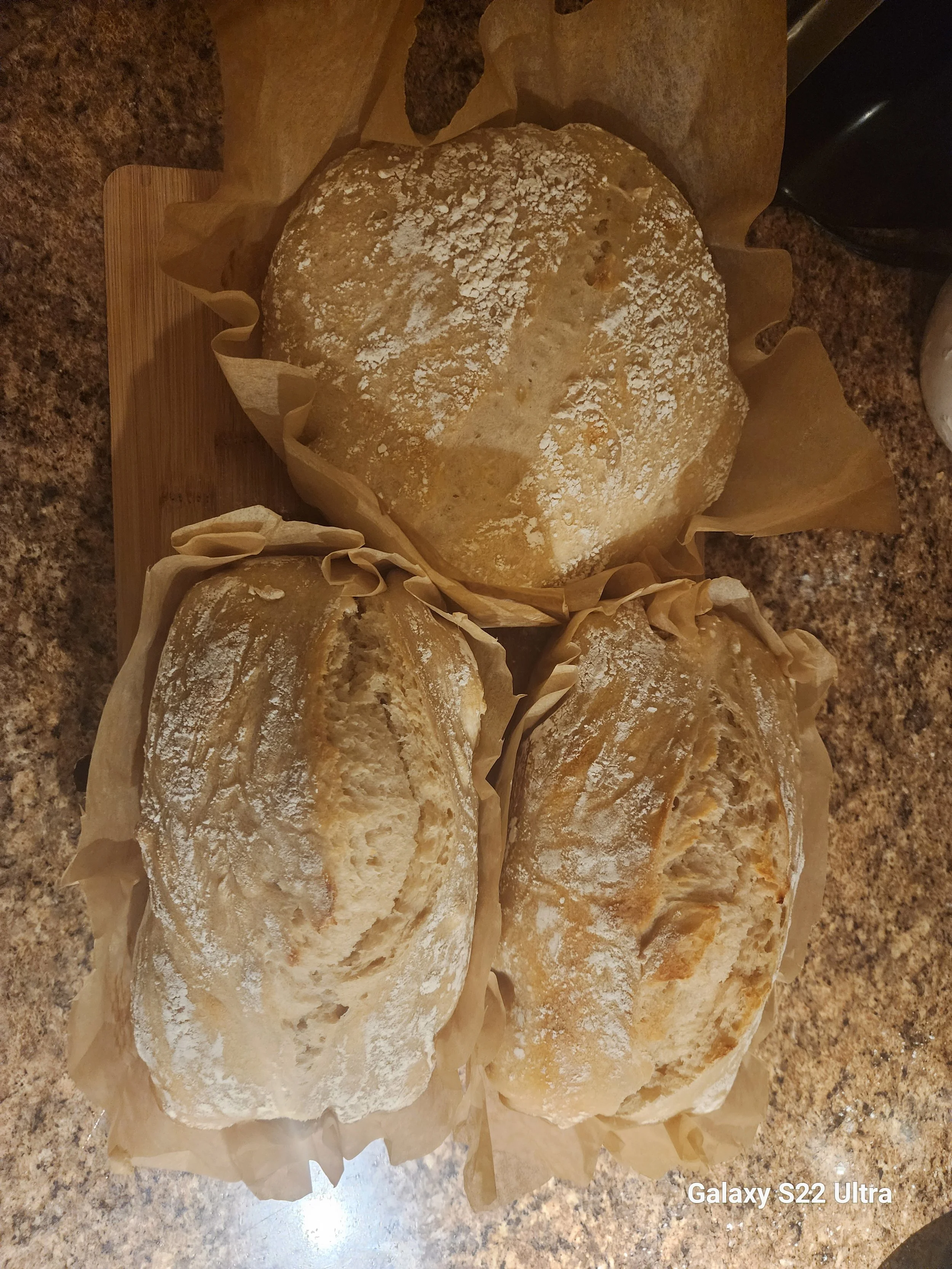 Freshly baked bread loaves with a dusting of flour, resting on parchment paper on a kitchen countertop.