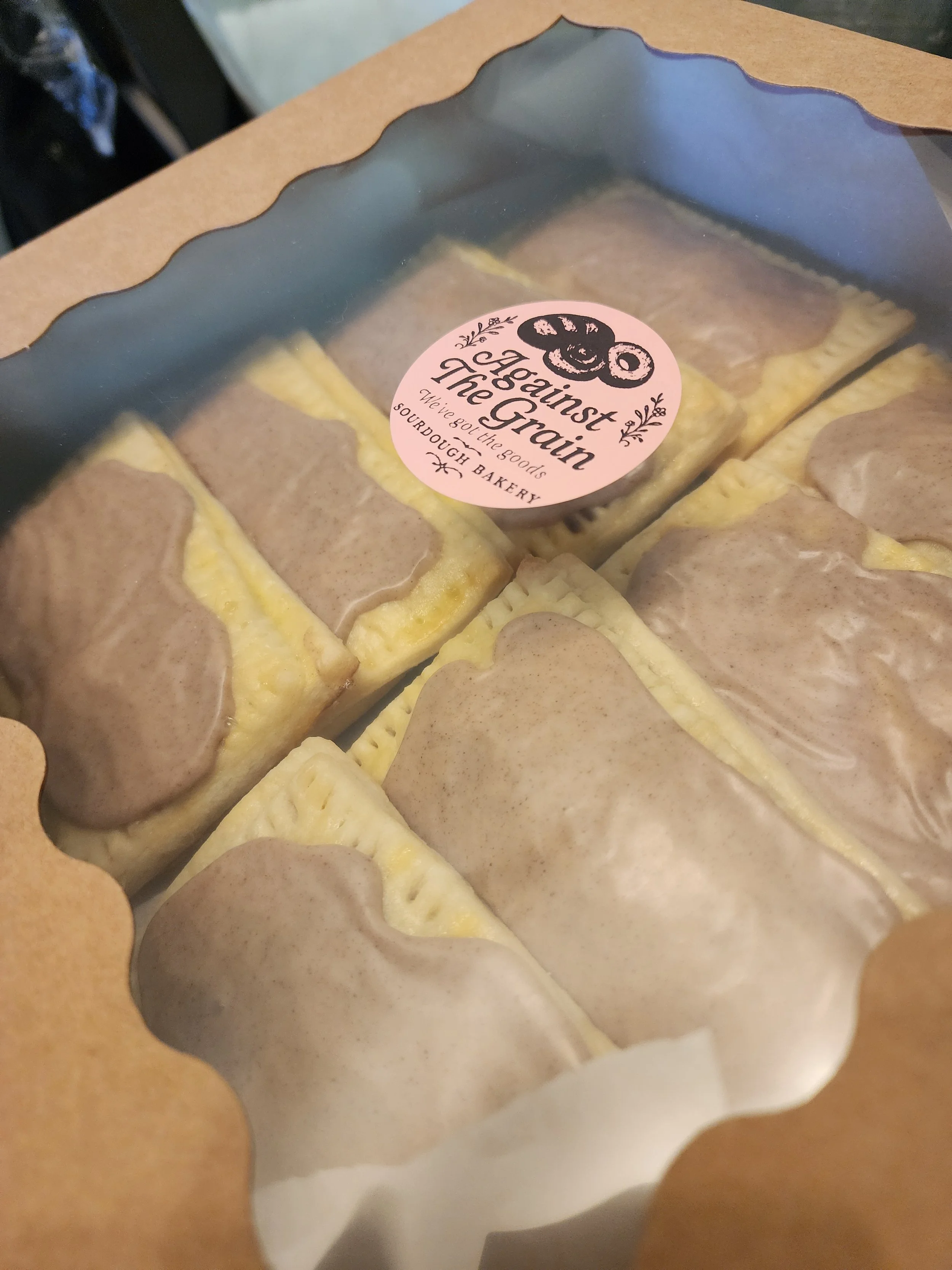 Box of assorted baked goods from a bakery, labeled 'The Greatest Bakes' with a pink sticker.
