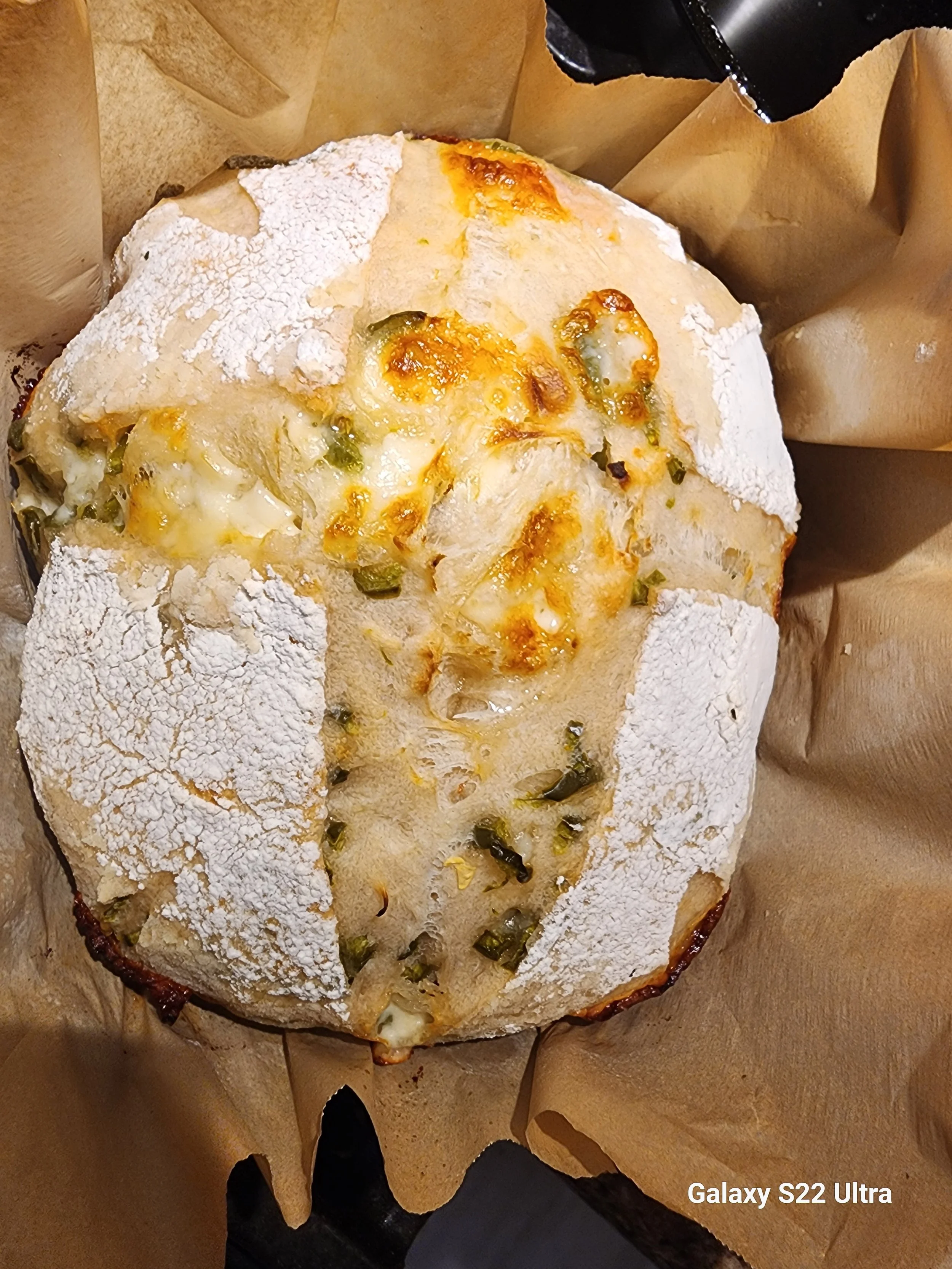 A pizza topped with melted cheese, green peppers, and possibly onions, with a thick crust, on parchment paper.