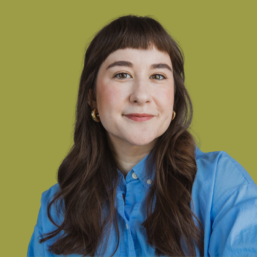 Portrait of a woman with brown hair and bangs, wearing a blue shirt and gold earrings, against a green background.
