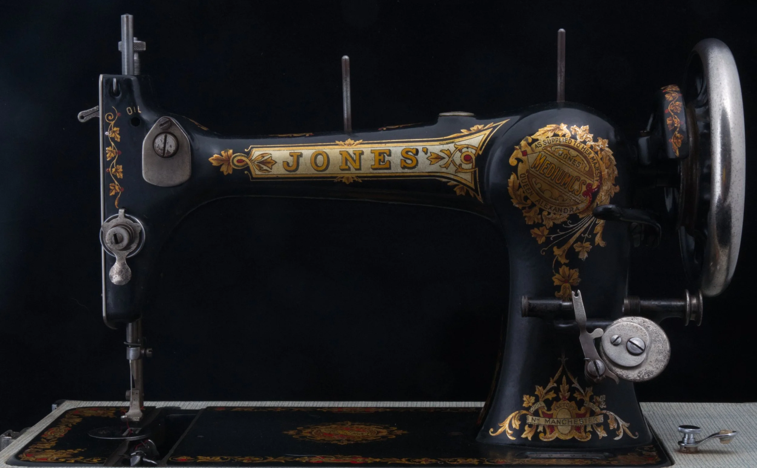 An antique black sewing machine with gold ornate details and the word 'JONES' painted on its side, set against a dark background.