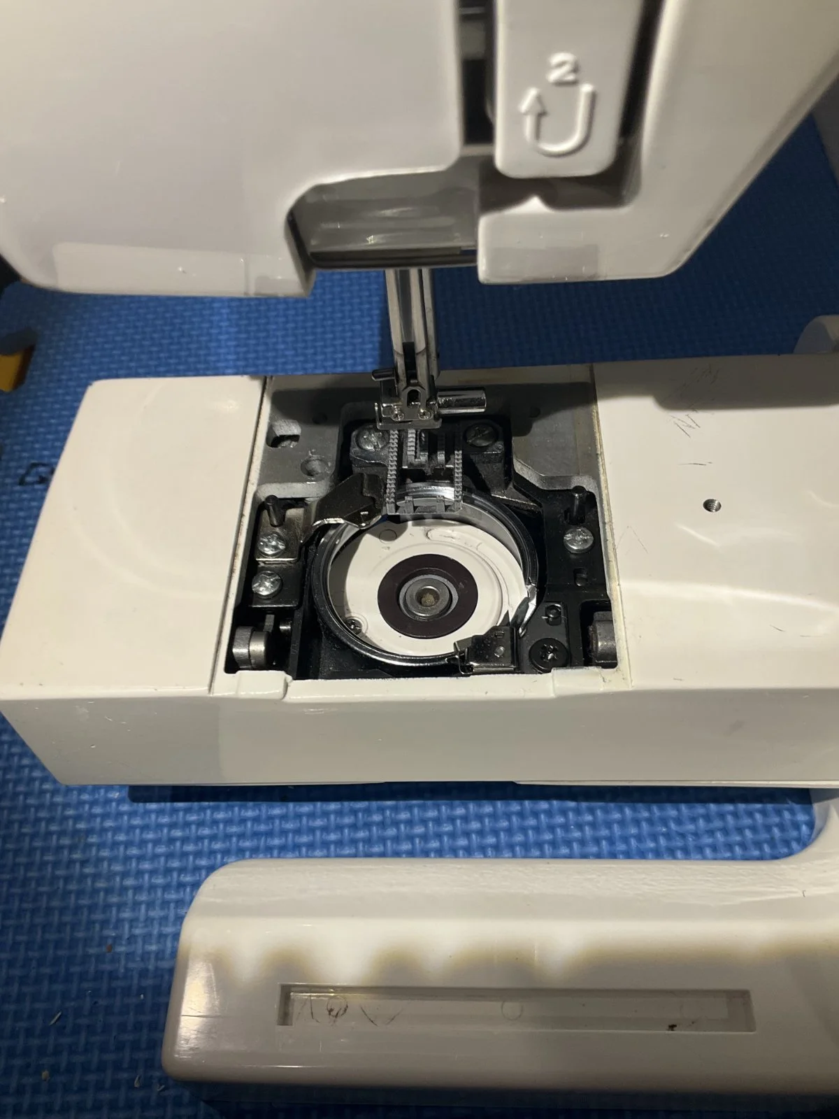 Close-up of a damaged or disassembled sewing machine, revealing internal mechanisms and a missing or broken part.