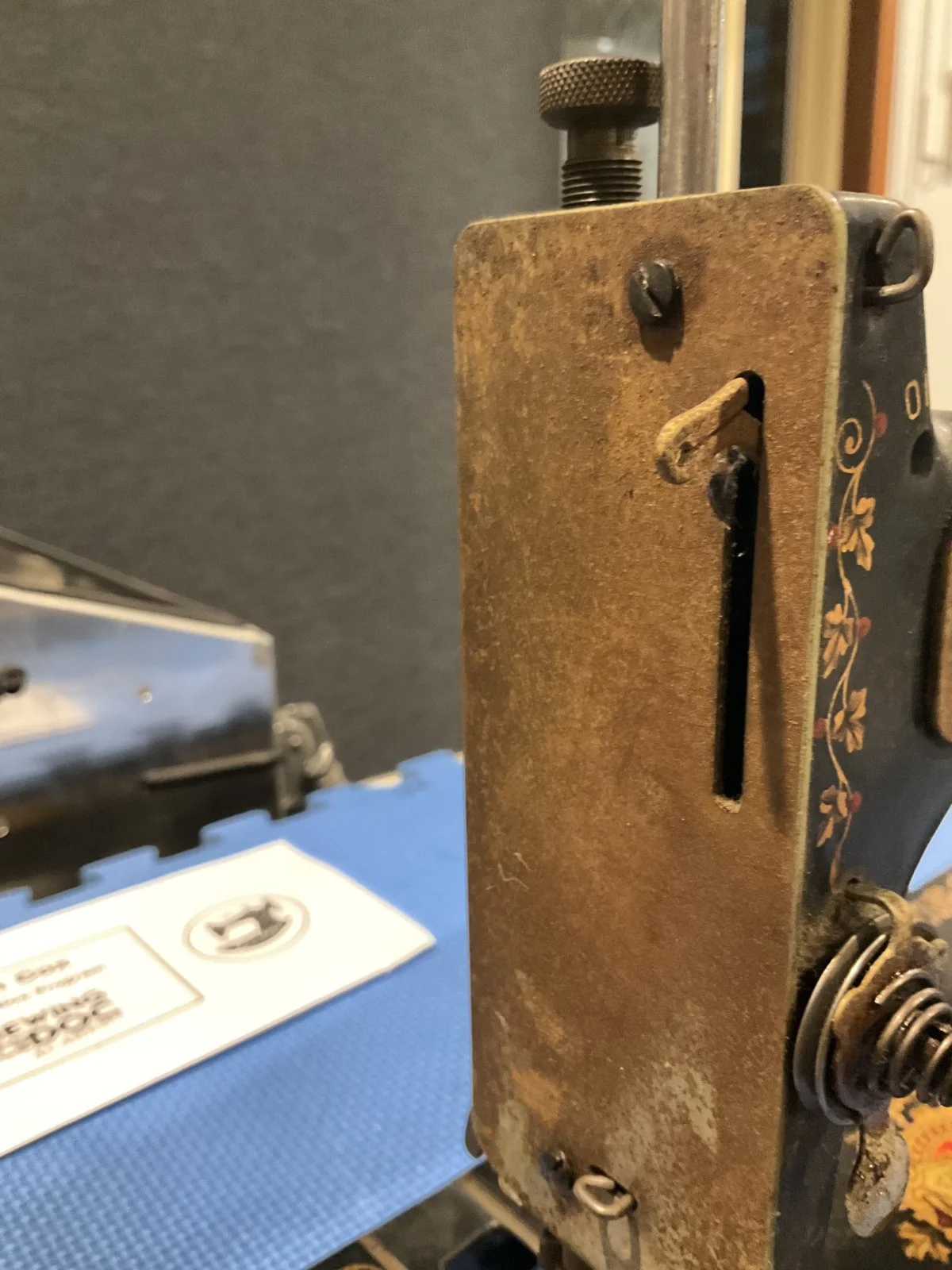 Close-up of an antique sewing machine with a rusted metal body and floral design on the side, in front of a blue box and papers.