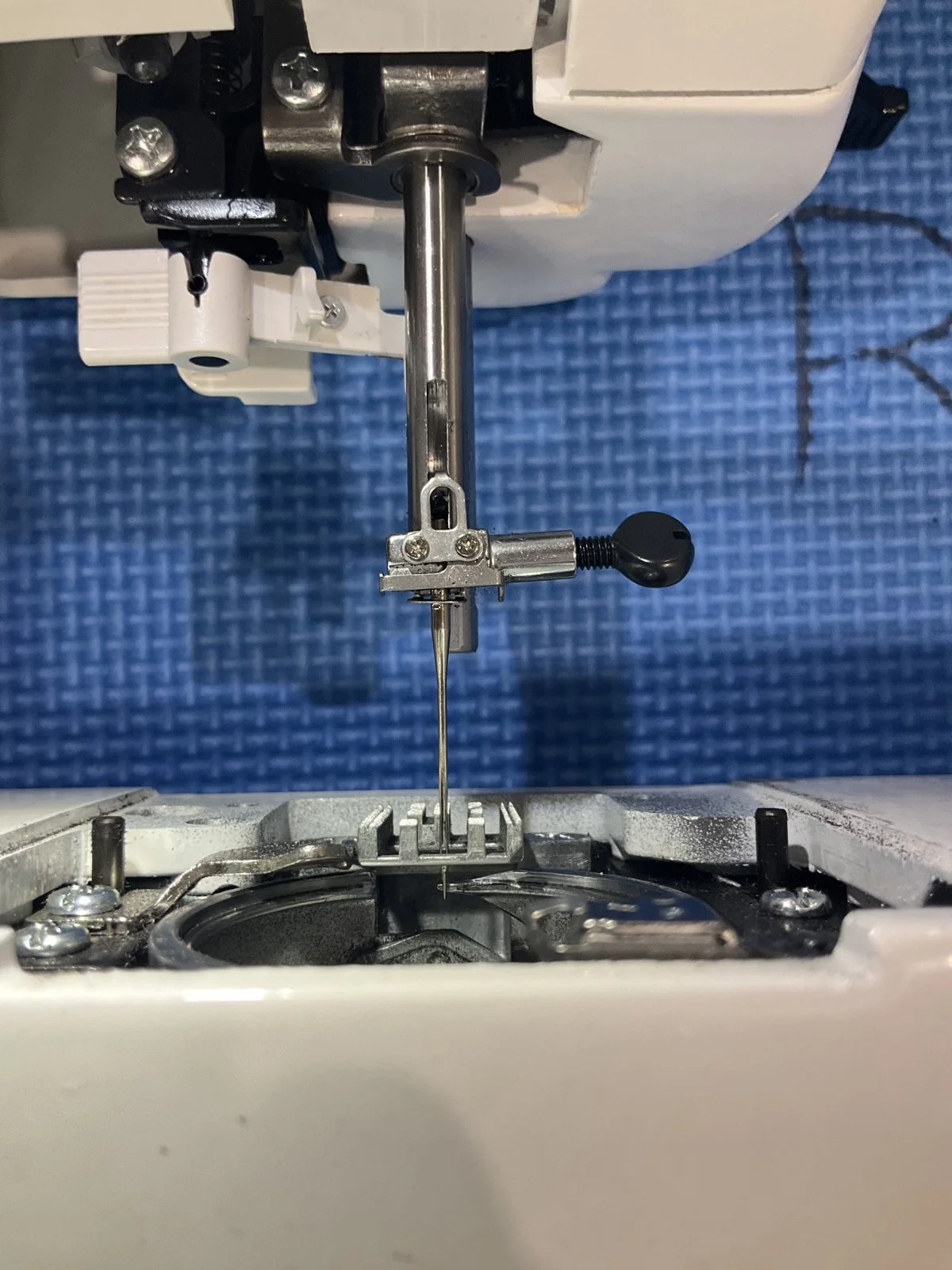 Close-up of the needle, arm, and bobbin area of a sewing machine with blue textured background.