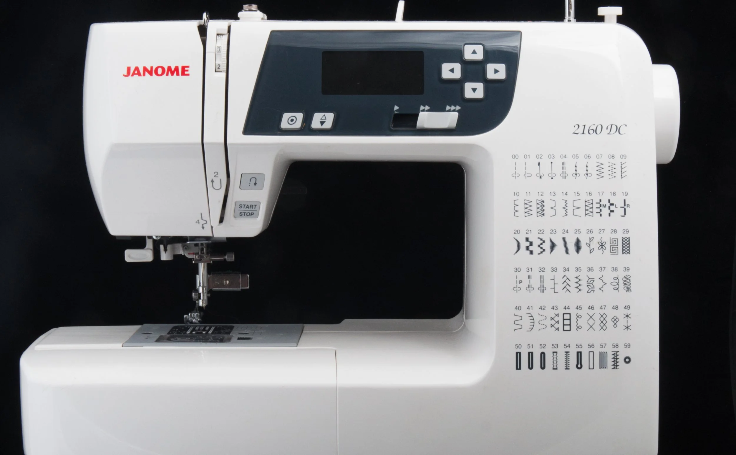 A Janome 2160 DC sewing machine with various stitch patterns displayed on the sewing surface, black background.