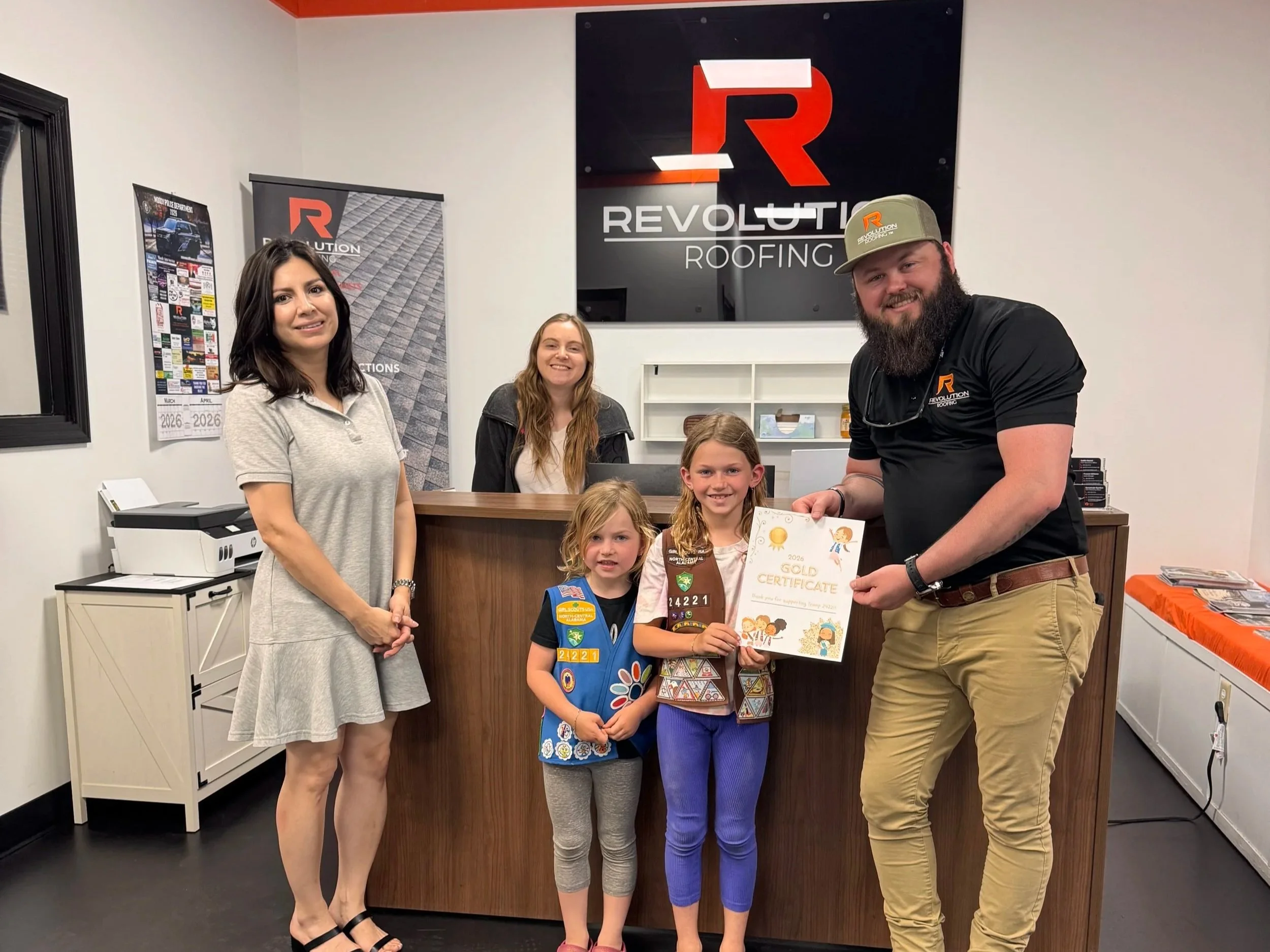 Group of five people standing together indoors, holding a plaque and certificate, in front of a sign that reads 'Revolution Roofing'.