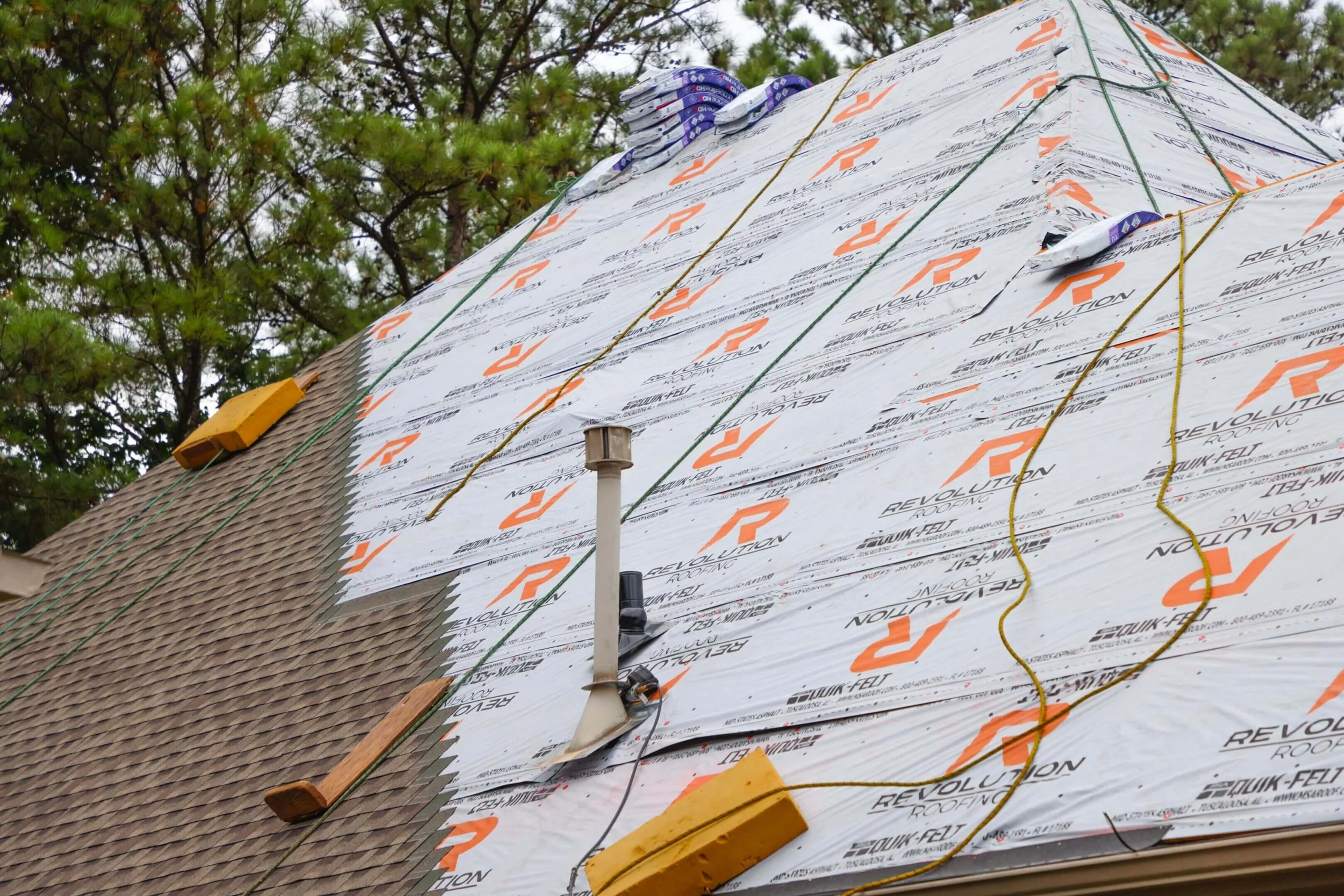 Roof under construction with underlayment and insulation materials, covered with Revolution Roofing felt and shingles.