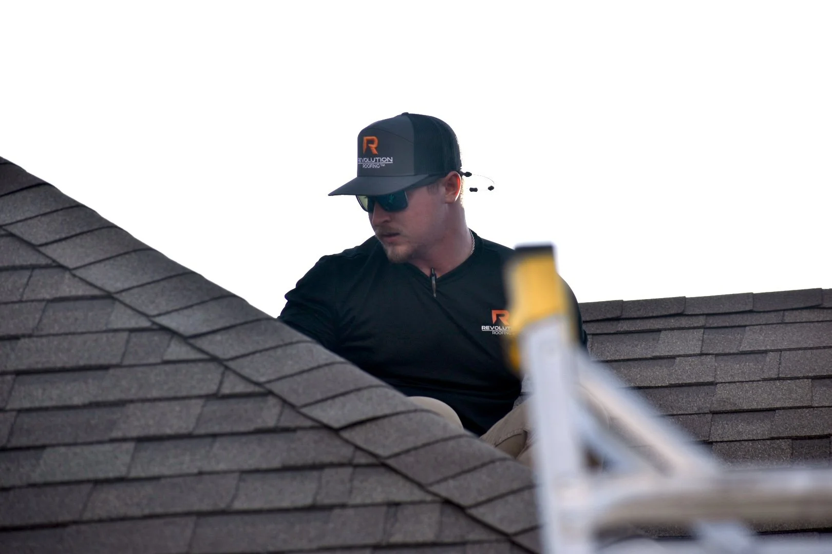 A roofing expert with Revolution Roofing working on a roof, wearing a black cap and sunglasses, with the logo 'Revolution Roofing' on his shirt and cap.