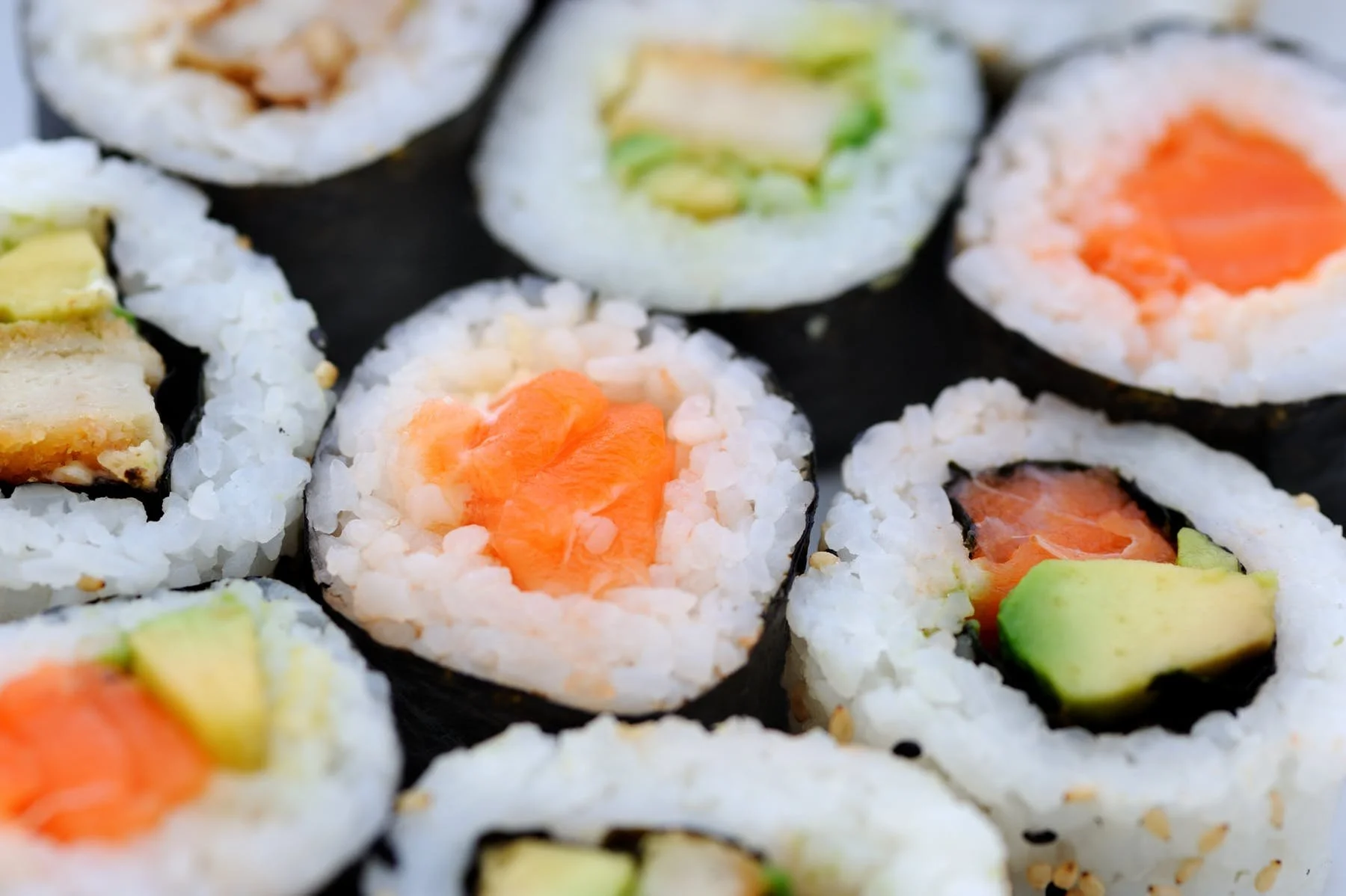 Close-up of assorted sushi rolls with fish, avocado, cucumber, and rice, wrapped in seaweed.
