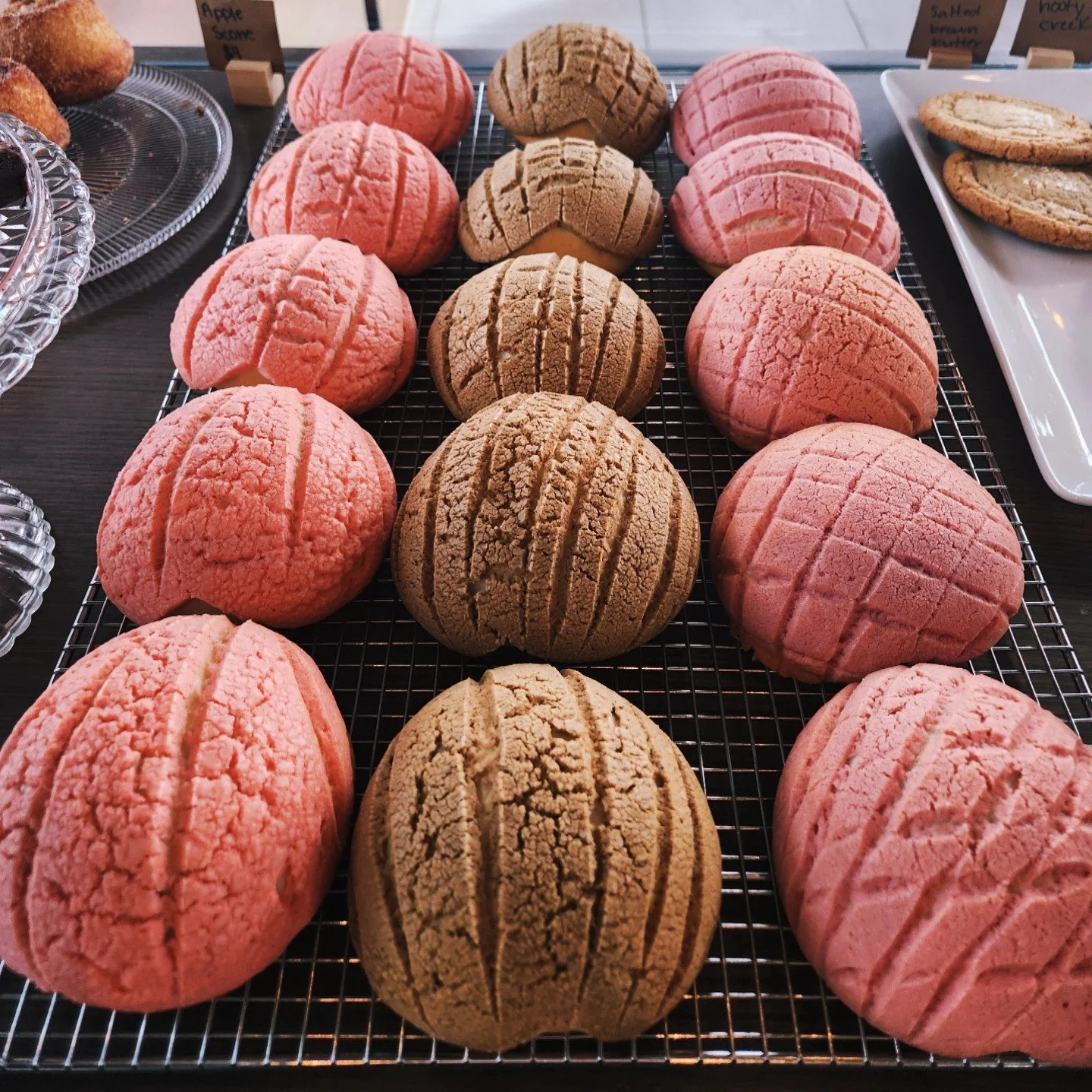 Pink and brown crinkle cookies arranged on a wire cooling rack at a bakery or cafe.