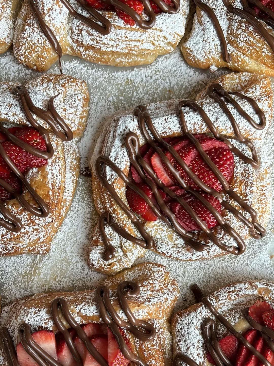 Delicious donuts topped with powdered sugar, sliced strawberries, and drizzled with chocolate.