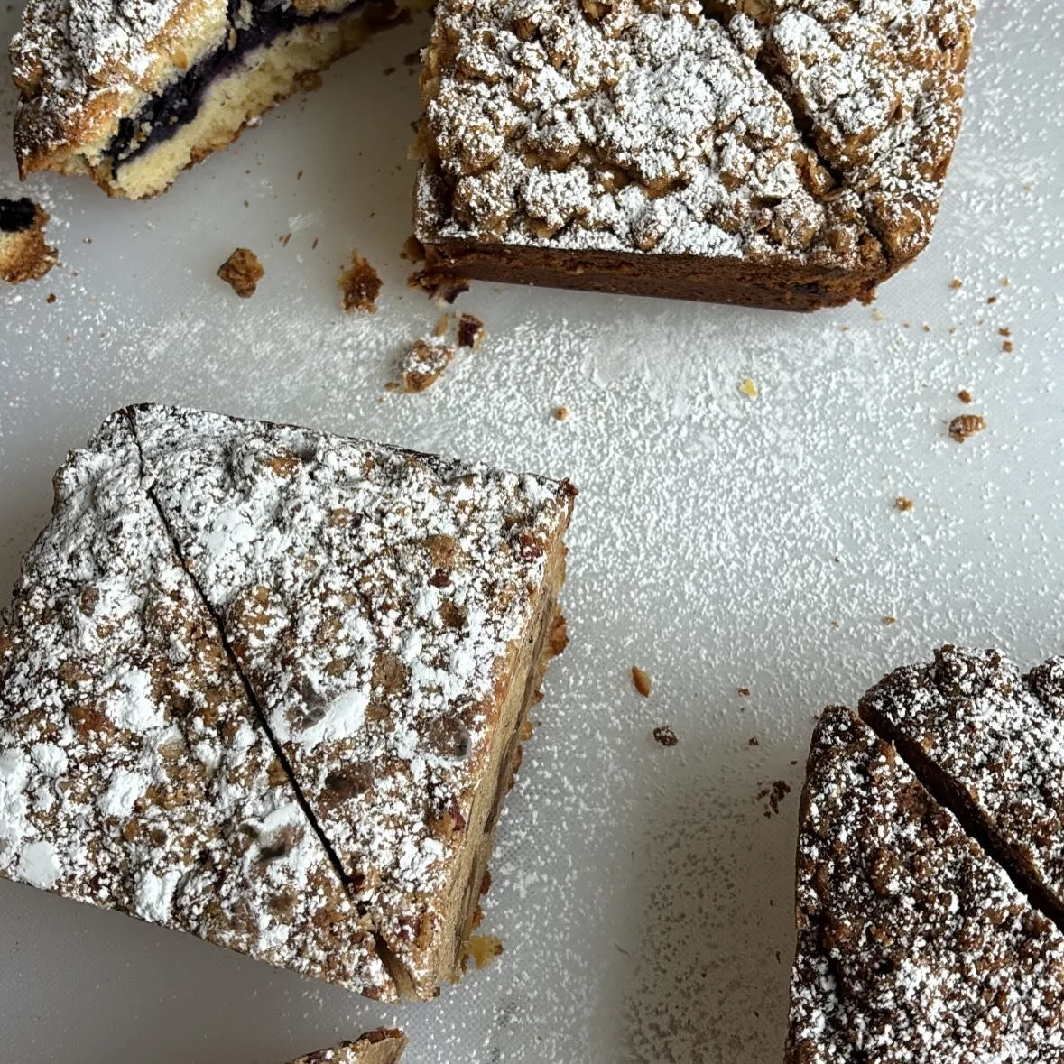 Pieces of chocolate cake with powdered sugar on top, on a white surface.