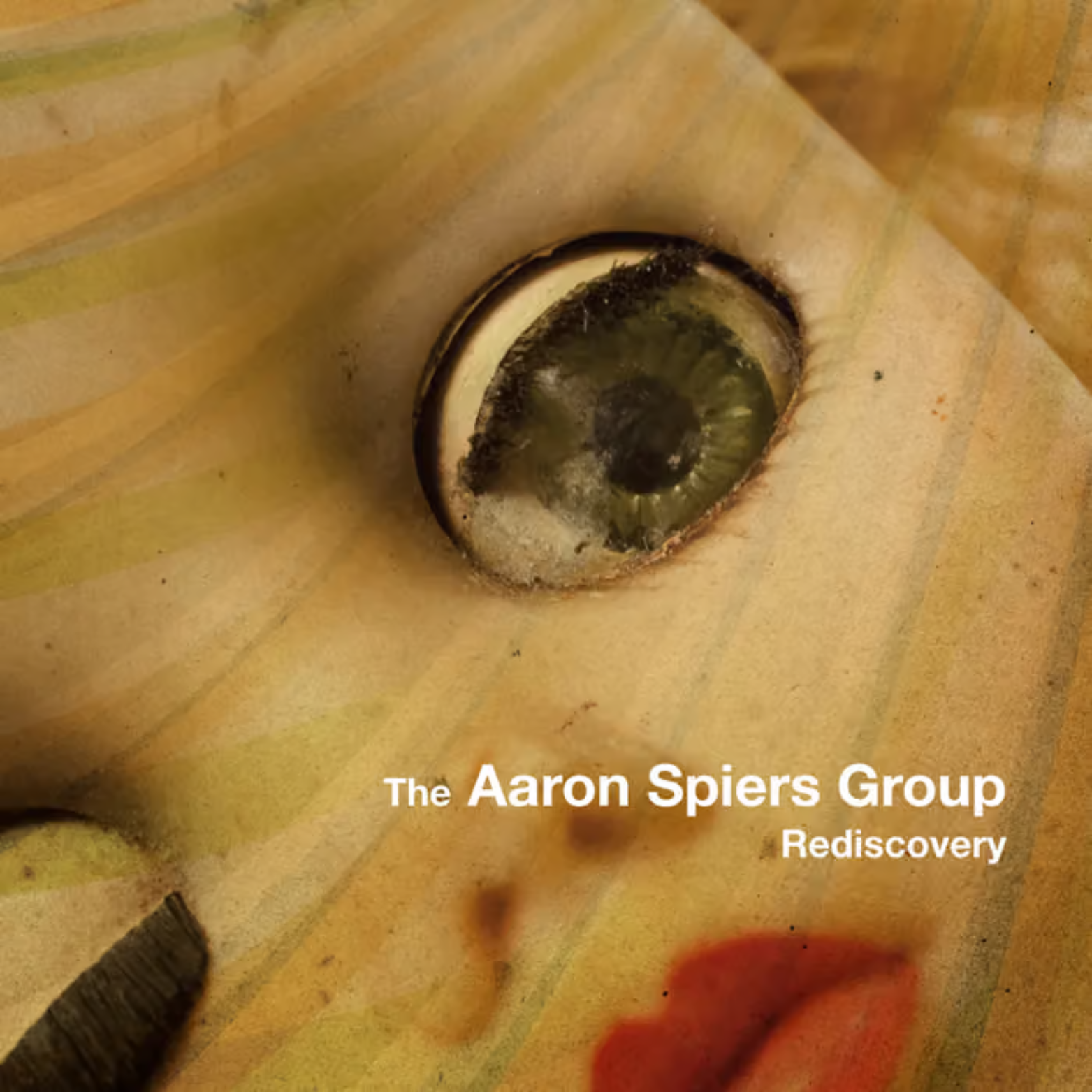Close-up of a burnt-out lightbulb socket on a wooden surface, with a piece of paper beneath it. The paper has the text 'The Aaron Spiers Group Rediscovery' printed on it.