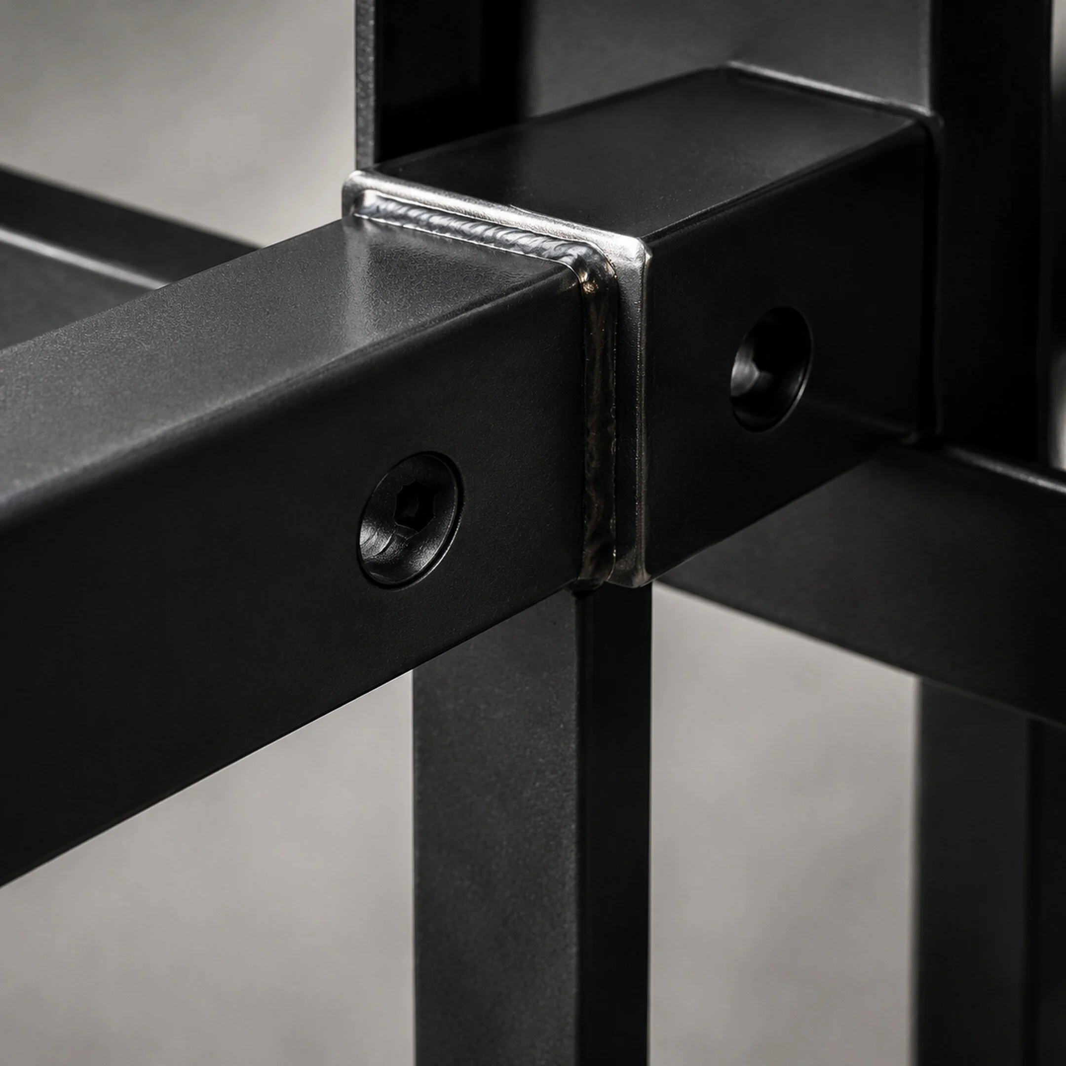 Close-up of a fabricated black steel corner joint with bolts and a clean welded connection.