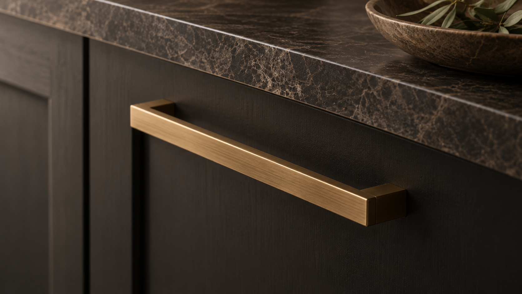 Brushed brass cabinet handle on dark bespoke cabinetry with marble worktop