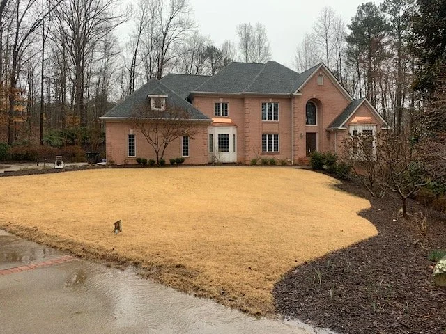 Large brick house with a well-maintained front yard and a curved driveway, surrounded by trees.