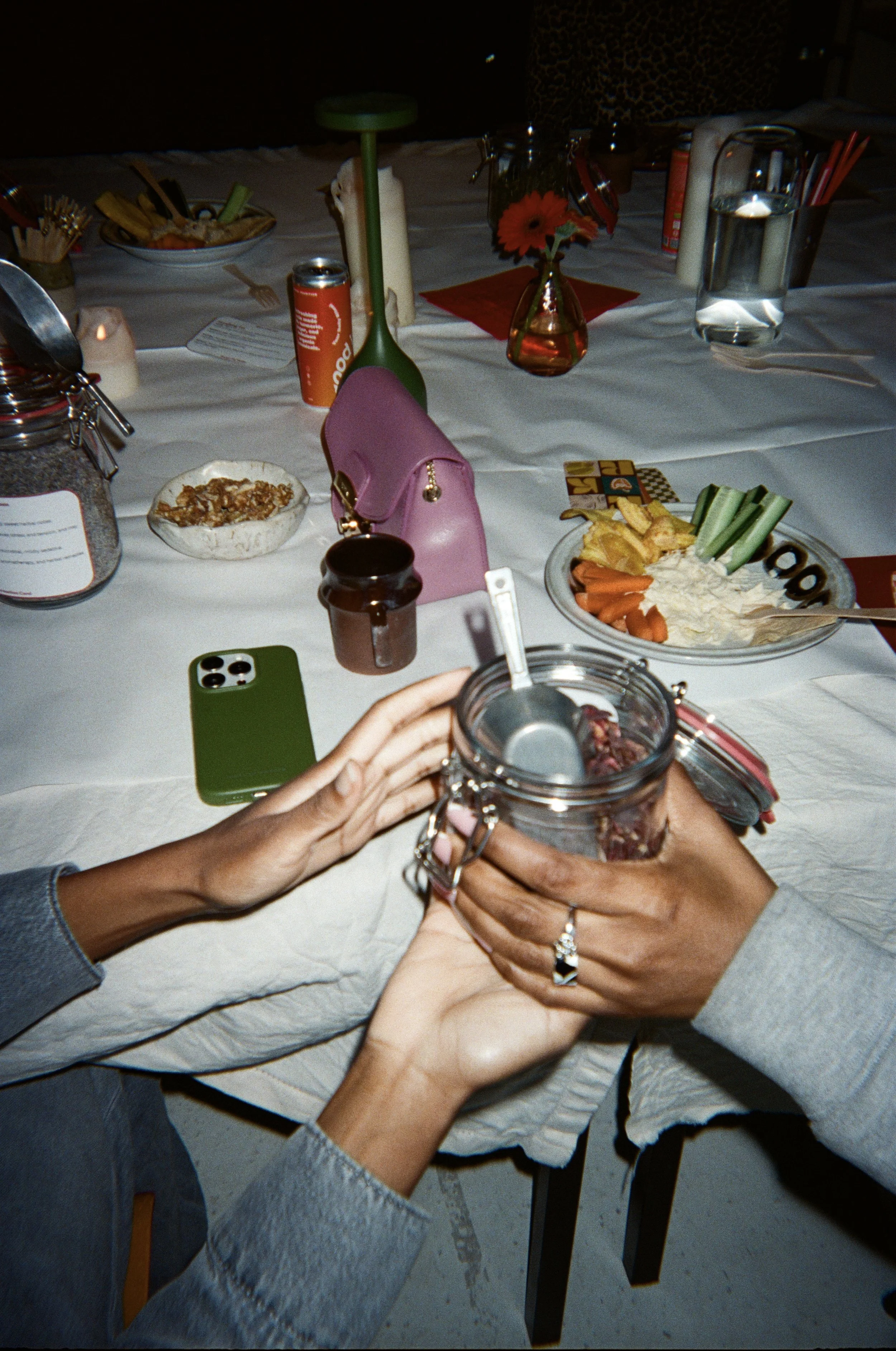 People holding a glass jar with a beverage at a dining table with various food dishes, drinks, and decorations.