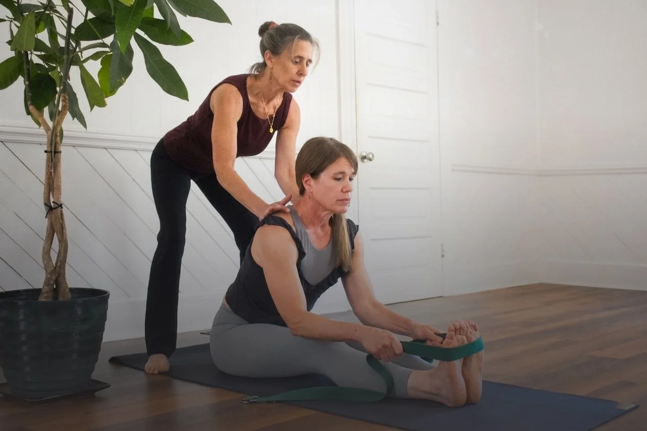 Lexie working with a student in a yoga studio by assisting with their posture.