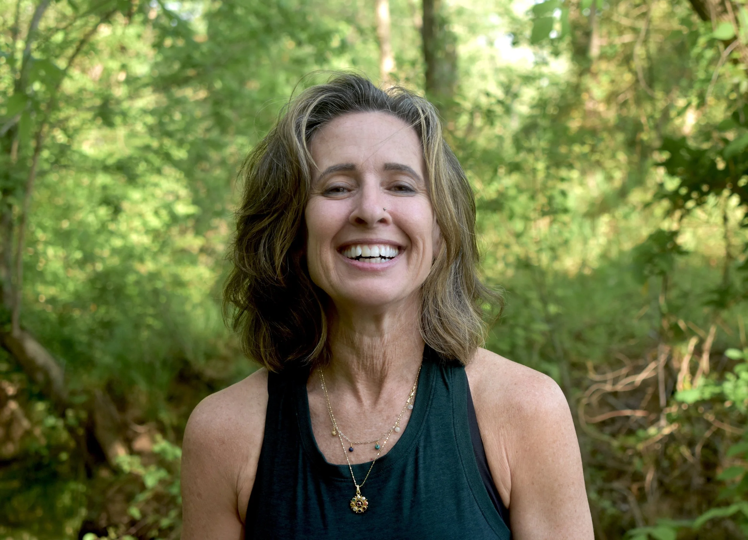 Close-up of Lexie smiling outdoors in a forest with green foliage background.