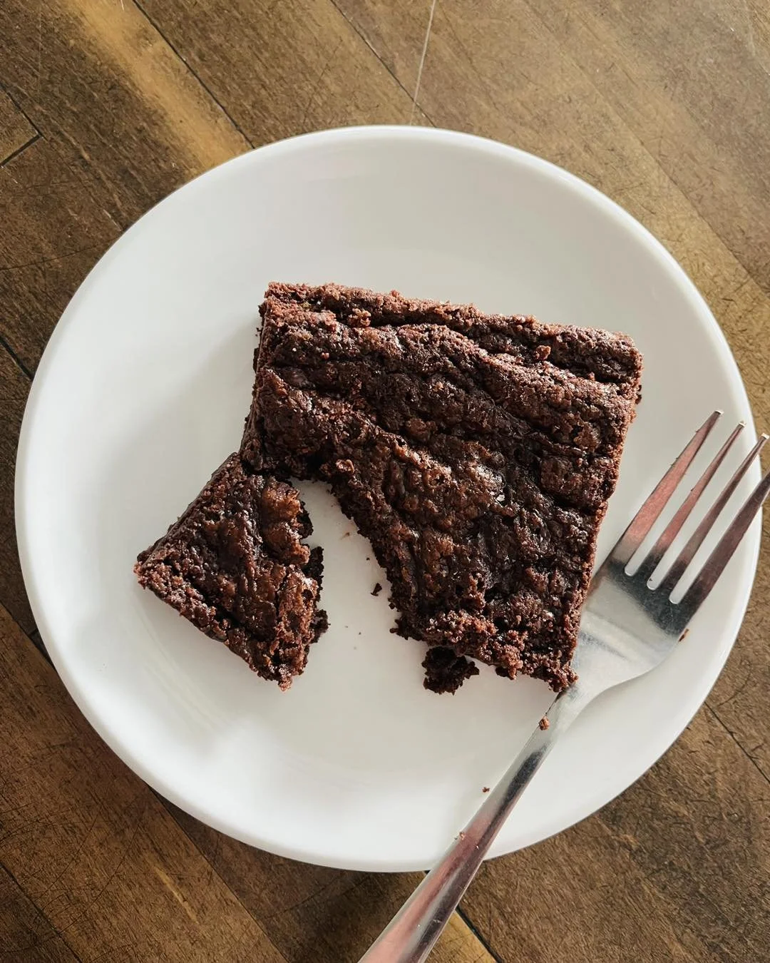 A piece of chocolate cake on a white plate with a fork, on a wooden table.