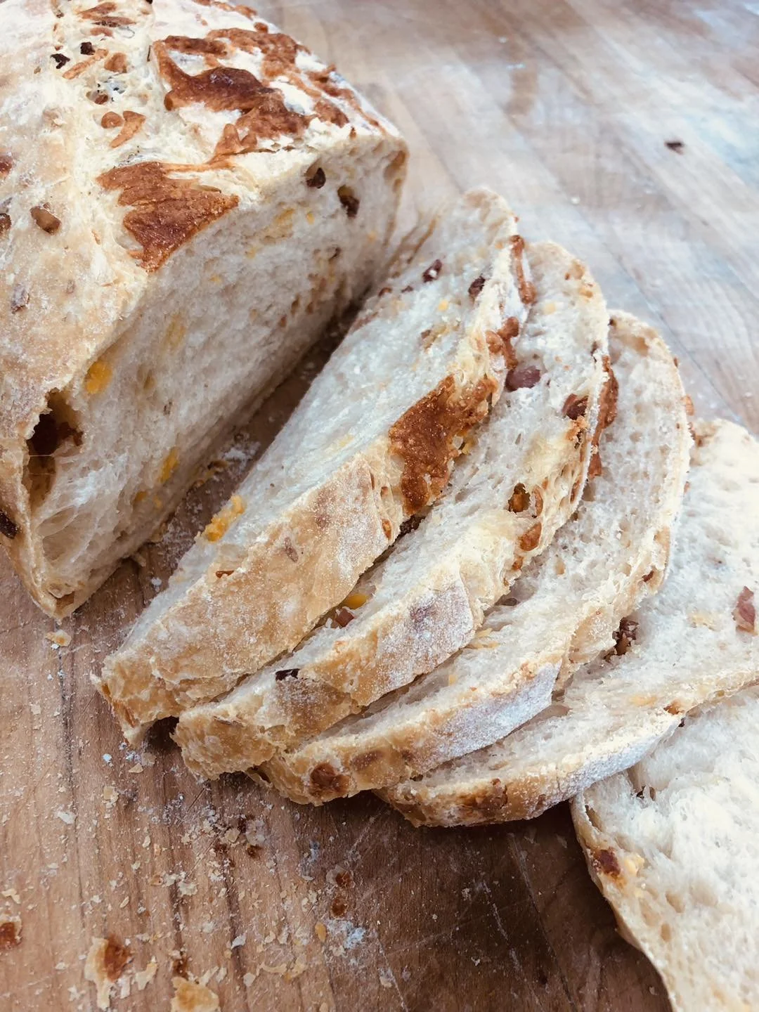 Sliced loaf of bread with a crusty top, placed on a wooden cutting board.
