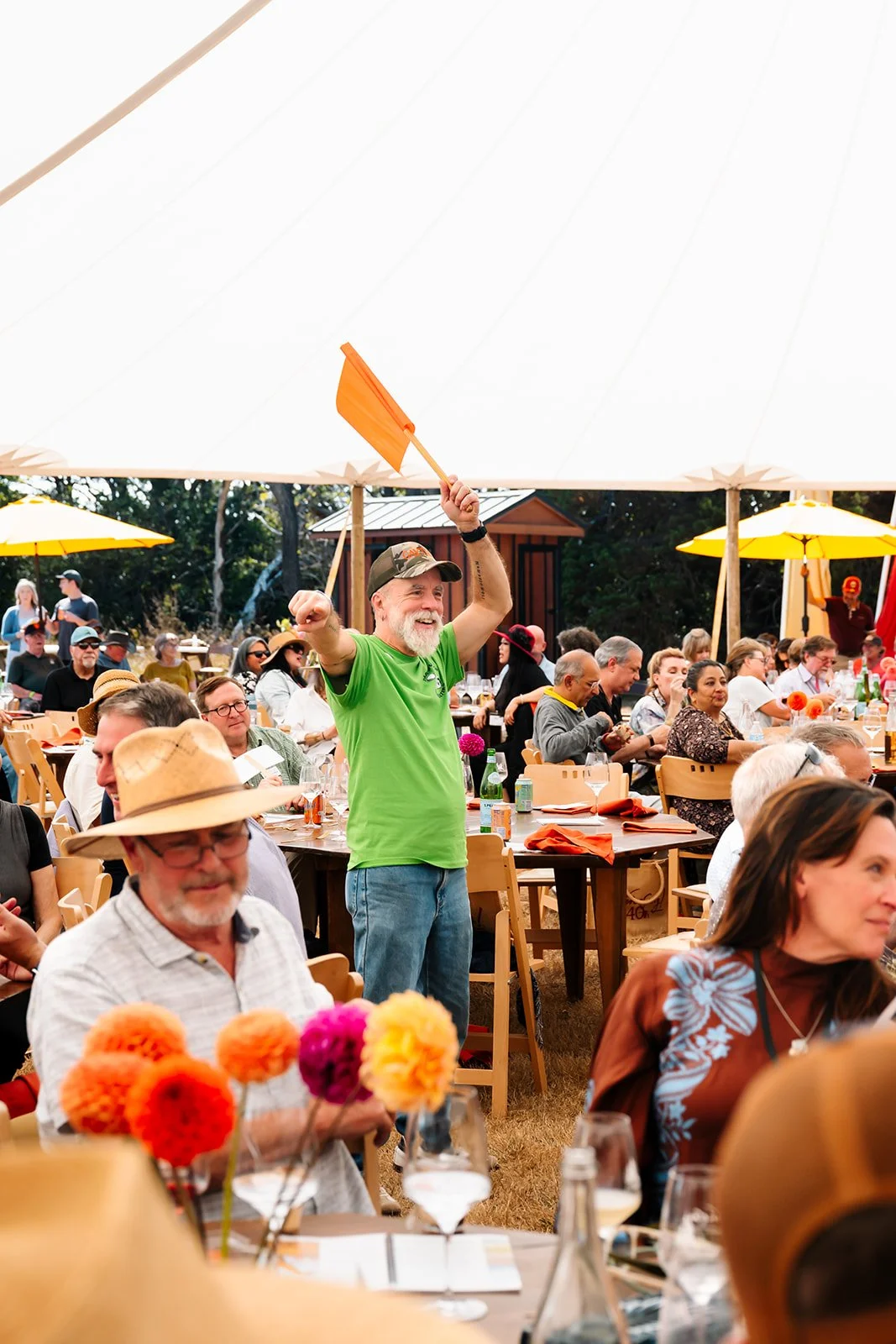 Man in green shirt holidng up flag at live auction at live auction and lunch at Winesong Wine Festival in Mendocino and Fort Bragg, California