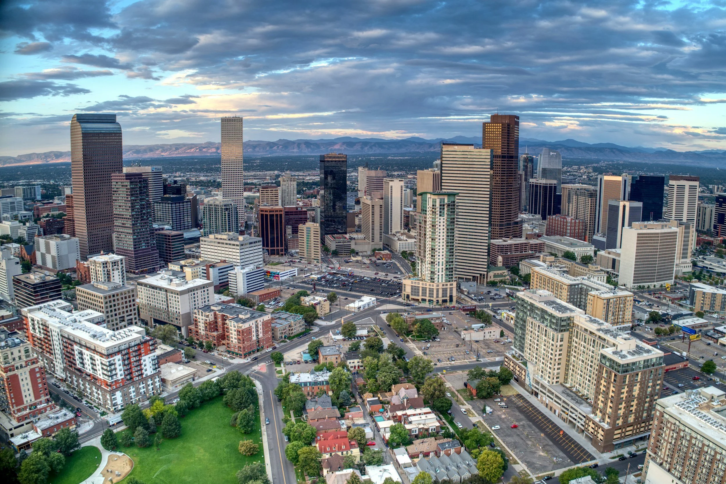 Aerial view of downtown denver with tall skyscrapers, surrounding mountains, and a partly cloudy sky.