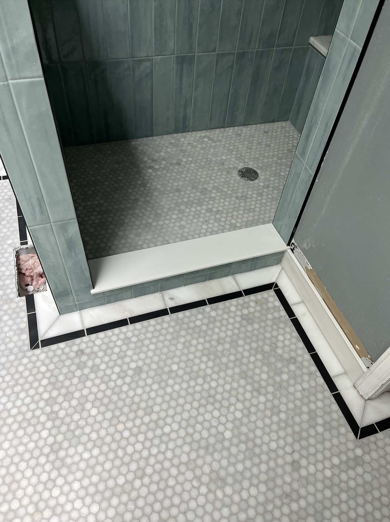 Empty shower stall with green tiled walls, a drain in the floor, and a small built-in shelf.
