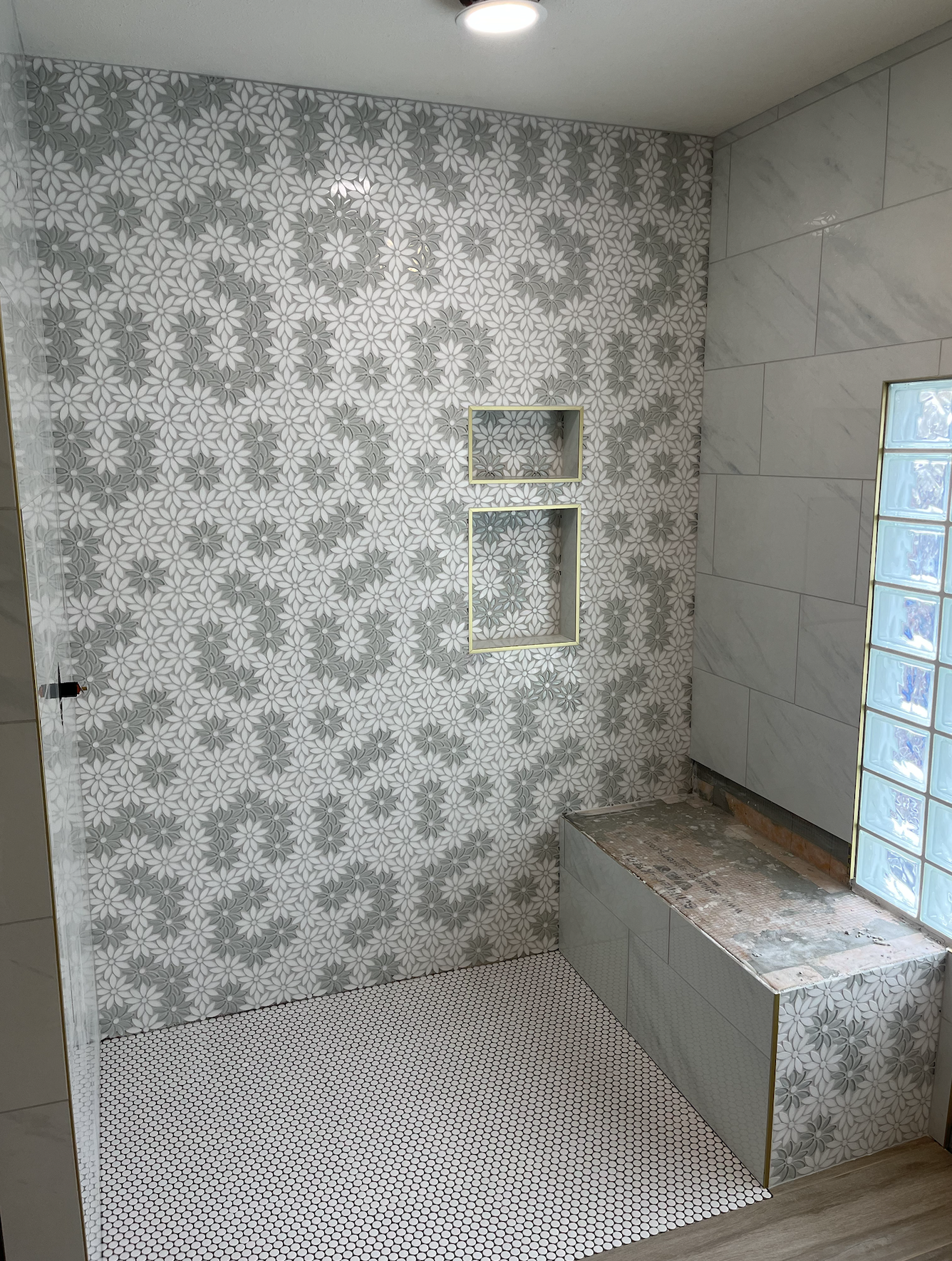 Bathroom under renovation with patterned tiles, a wall with glass blocks, and unfinished fixtures.