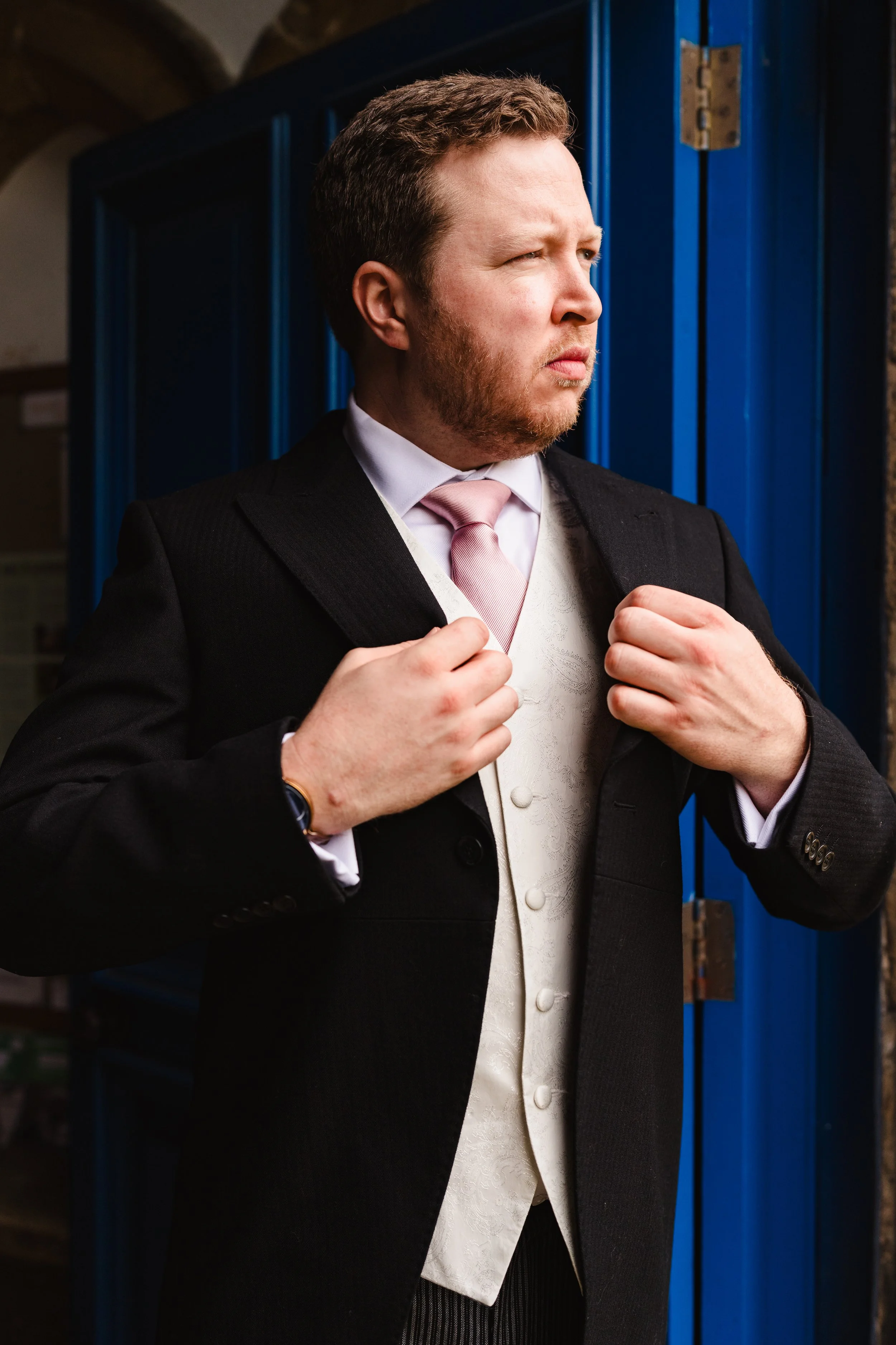 A man dressed in formal attire, adjusting his suit jacket in front of a blue locker.