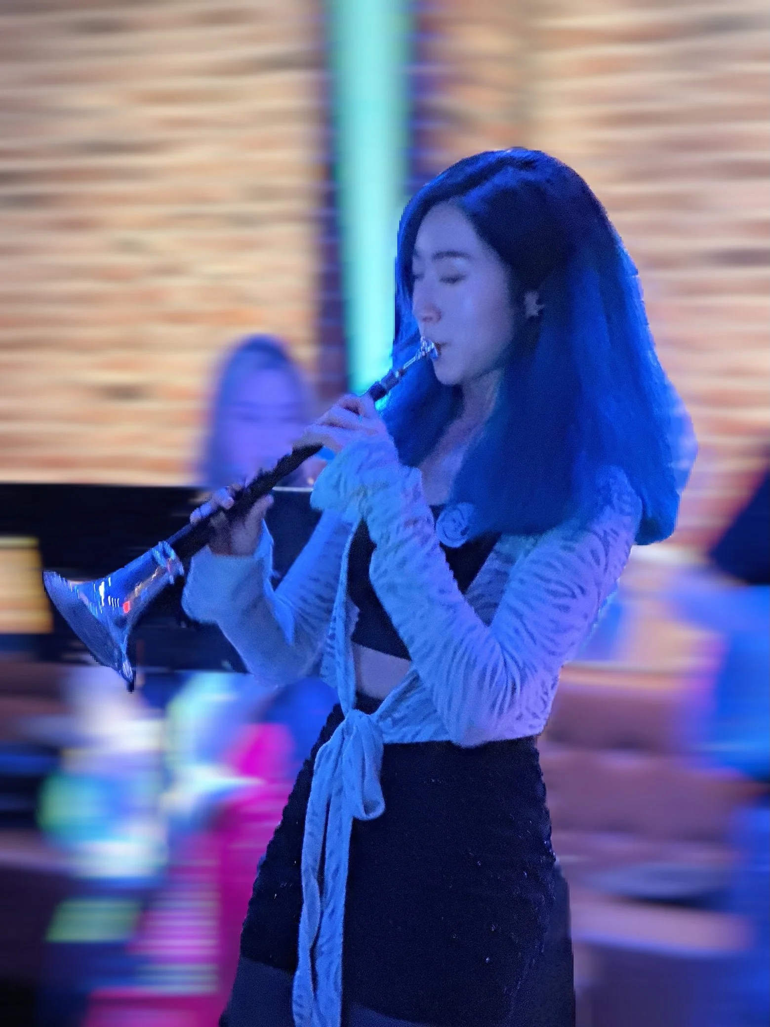 A woman with blue hair playing a saxophone in front of a colorful, blurred background.
