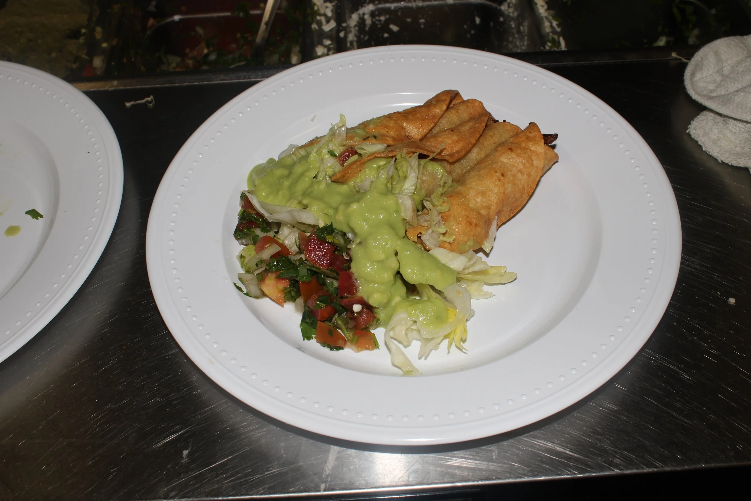 Plate of Mexican food with two crispy taquitos topped with guacamole, served with a side salad of chopped lettuce, tomatoes, and green onions.
